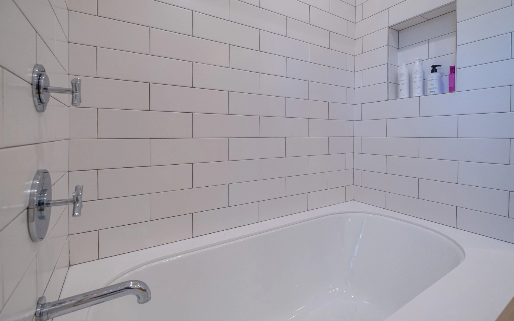 White subway tile tub surround with a recessed shower niche and chrome cross-handle valves in a Los Angeles ADU bathroom