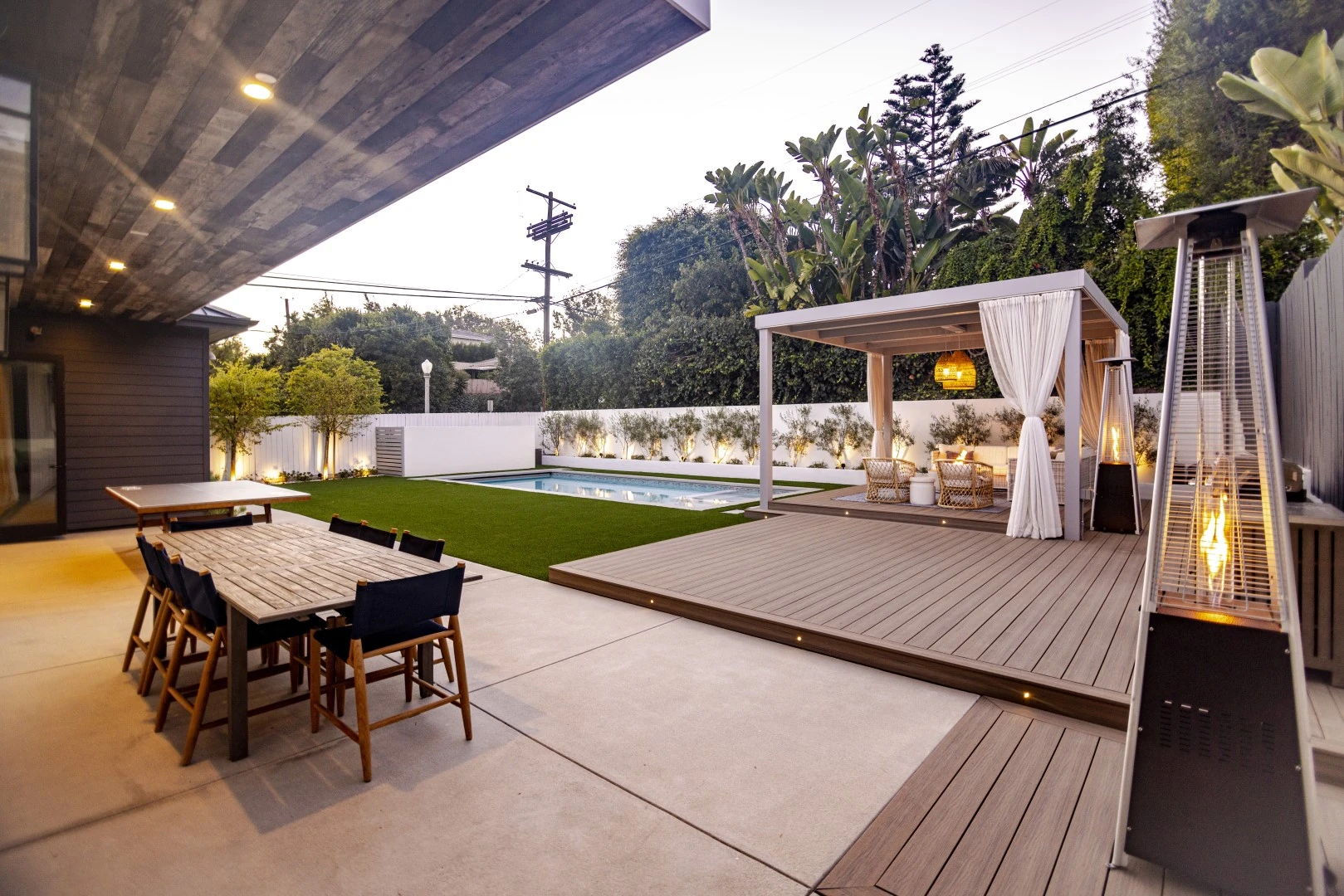 Ground-level composite deck in Los Angeles with built-in deck lights and a curtained pergola lounge overlooking a backyard pool