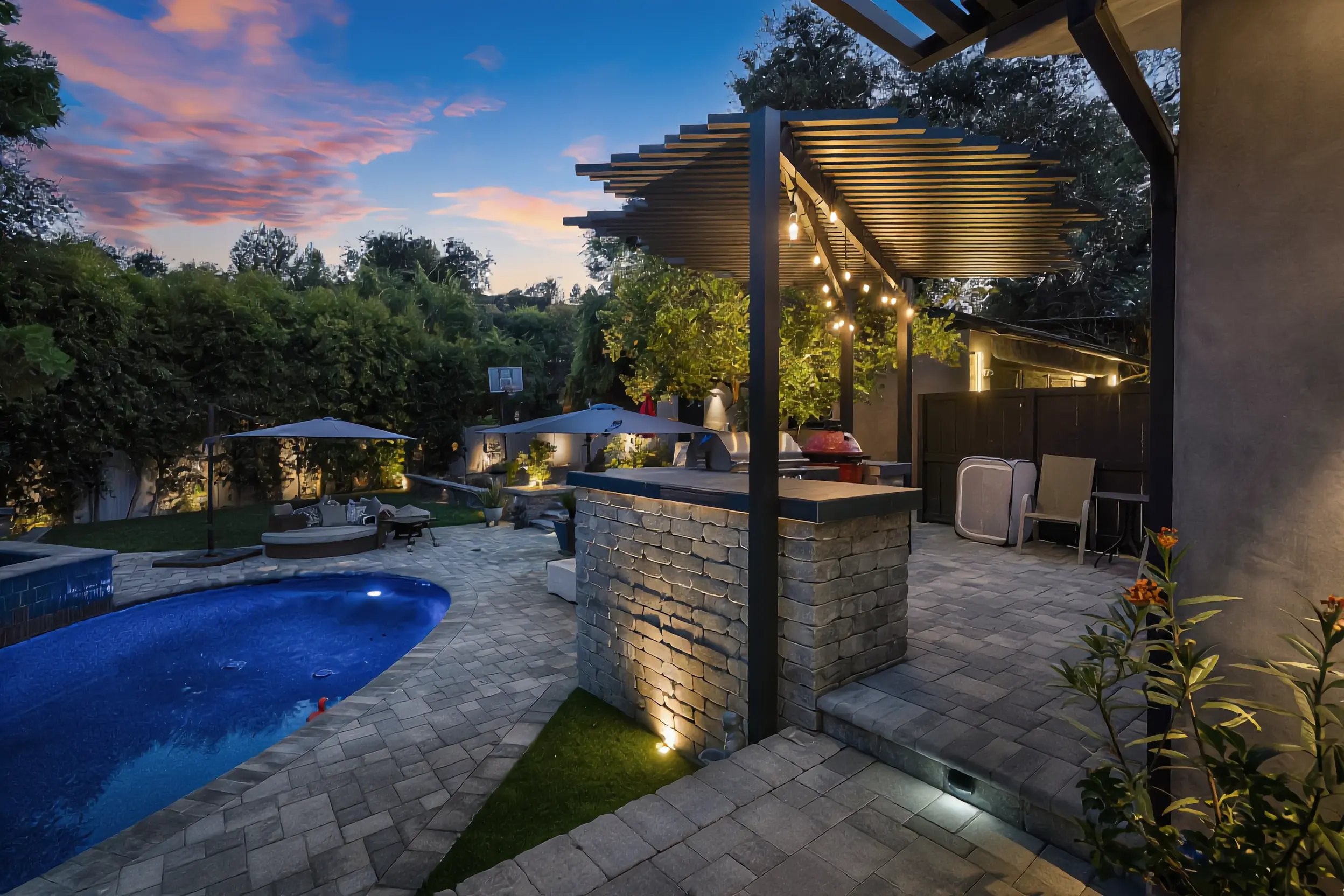 Modern black pergola over a stone outdoor kitchen beside a backyard pool