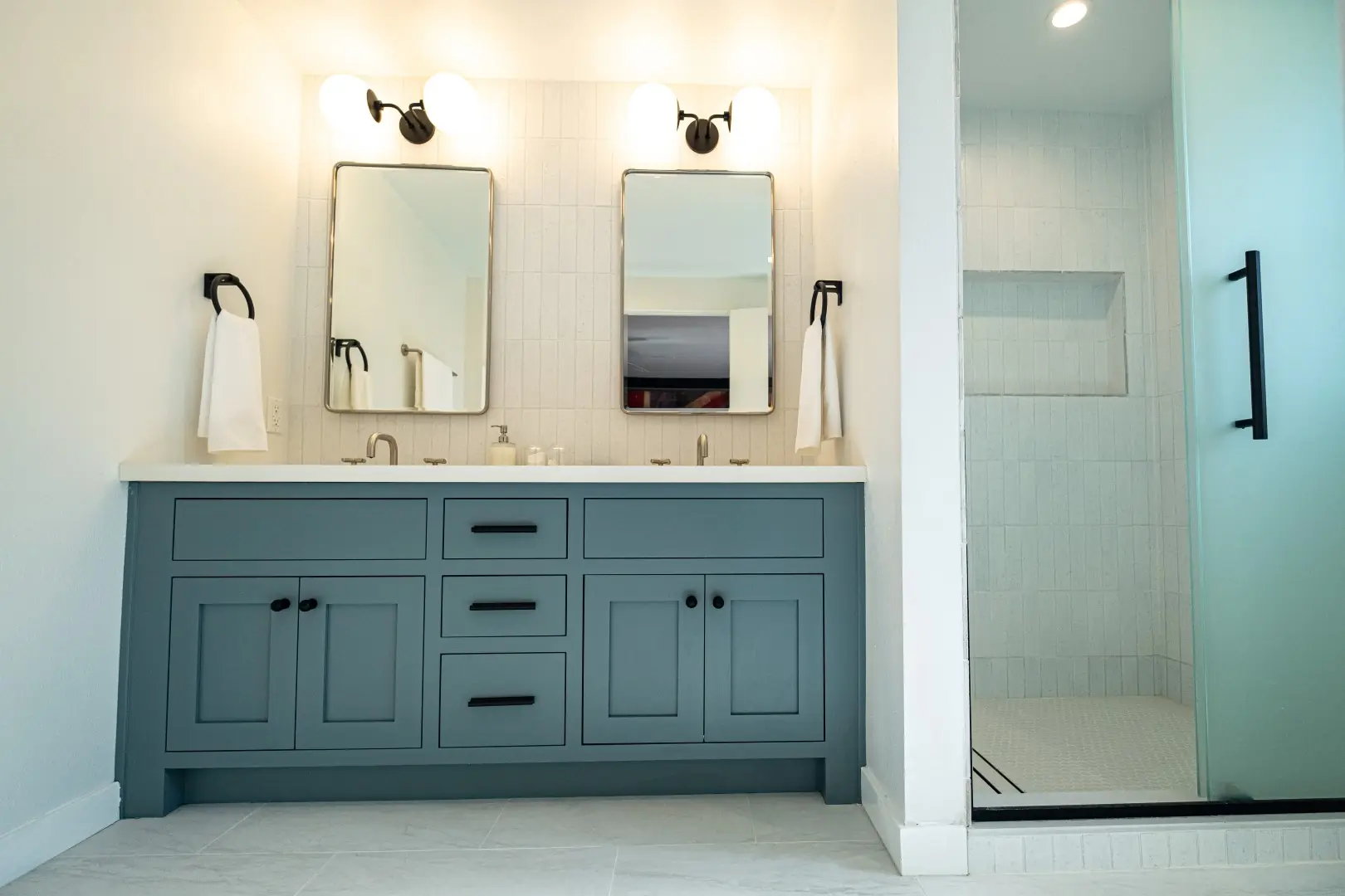 Bathroom remodel in Burbank with a blue-gray double vanity, white tile, black hardware, and a frosted glass shower