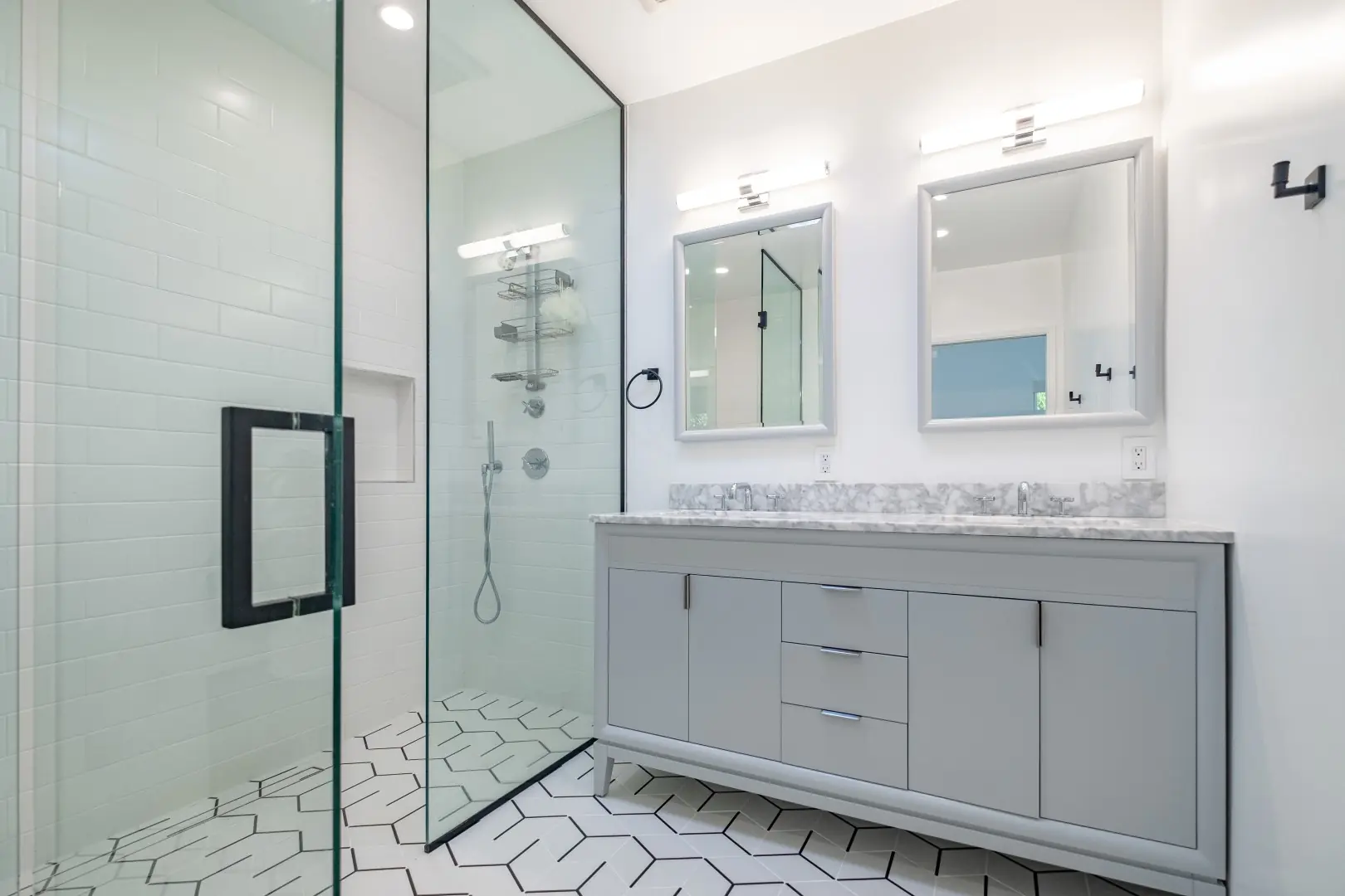 Bathroom remodel in Santa Monica with a gray double vanity, frameless glass shower, and white hexagon floor tile