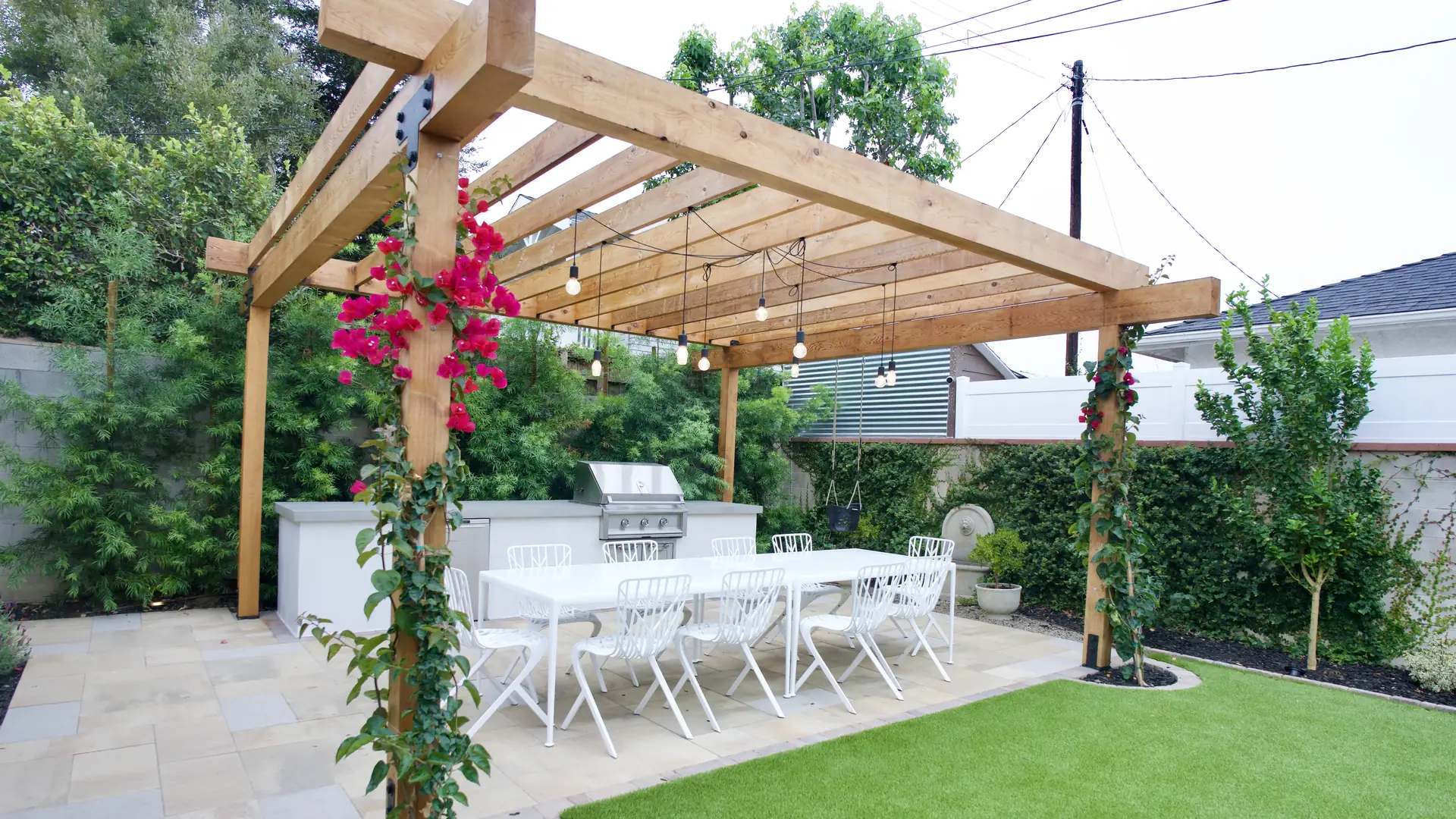Los Angeles outdoor living space with a cedar pergola wrapped in bougainvillea, string lights over a dining table, and a stainless steel outdoor kitchen