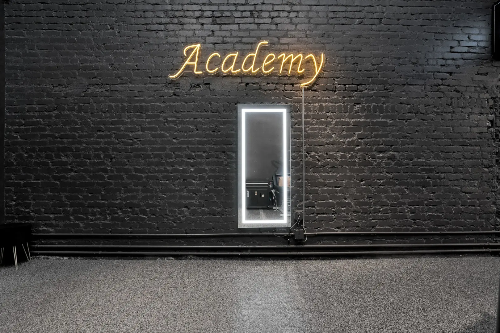 Cleopatra Tattoo academy area with a gold neon sign and a backlit mirror on painted brick in Santa Monica