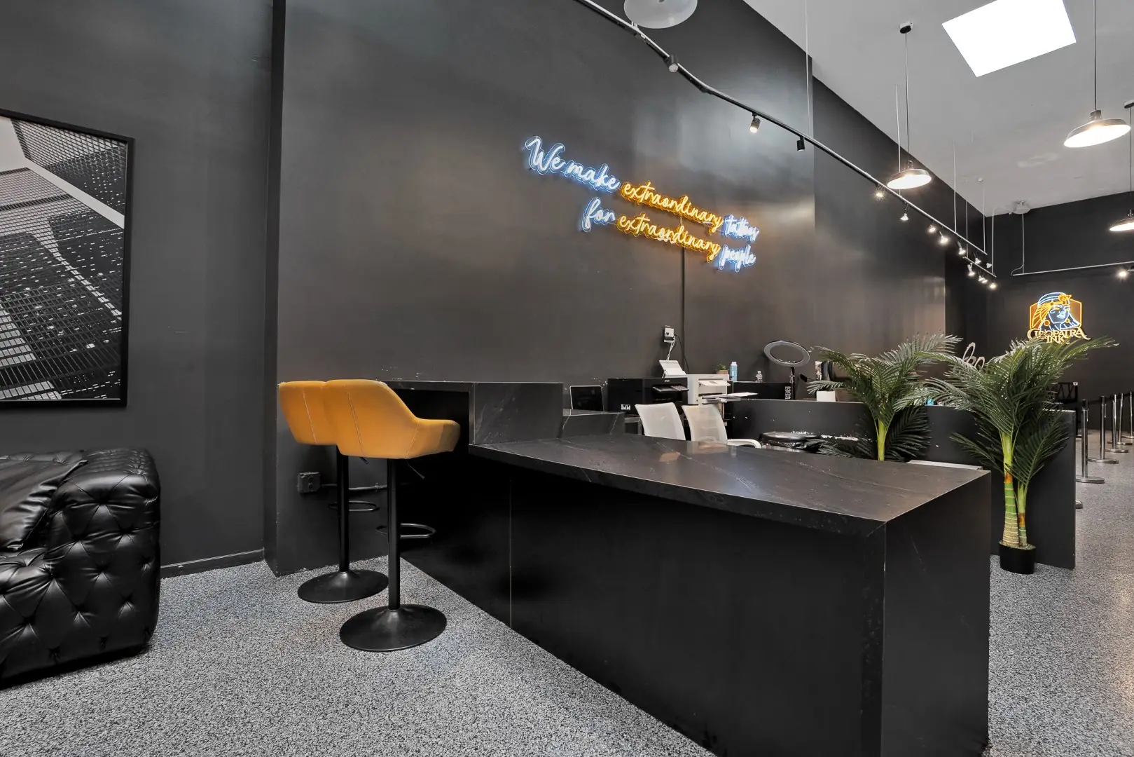 Cleopatra Tattoo consultation desk with a leather stool, neon lettering, and potted palms in Santa Monica