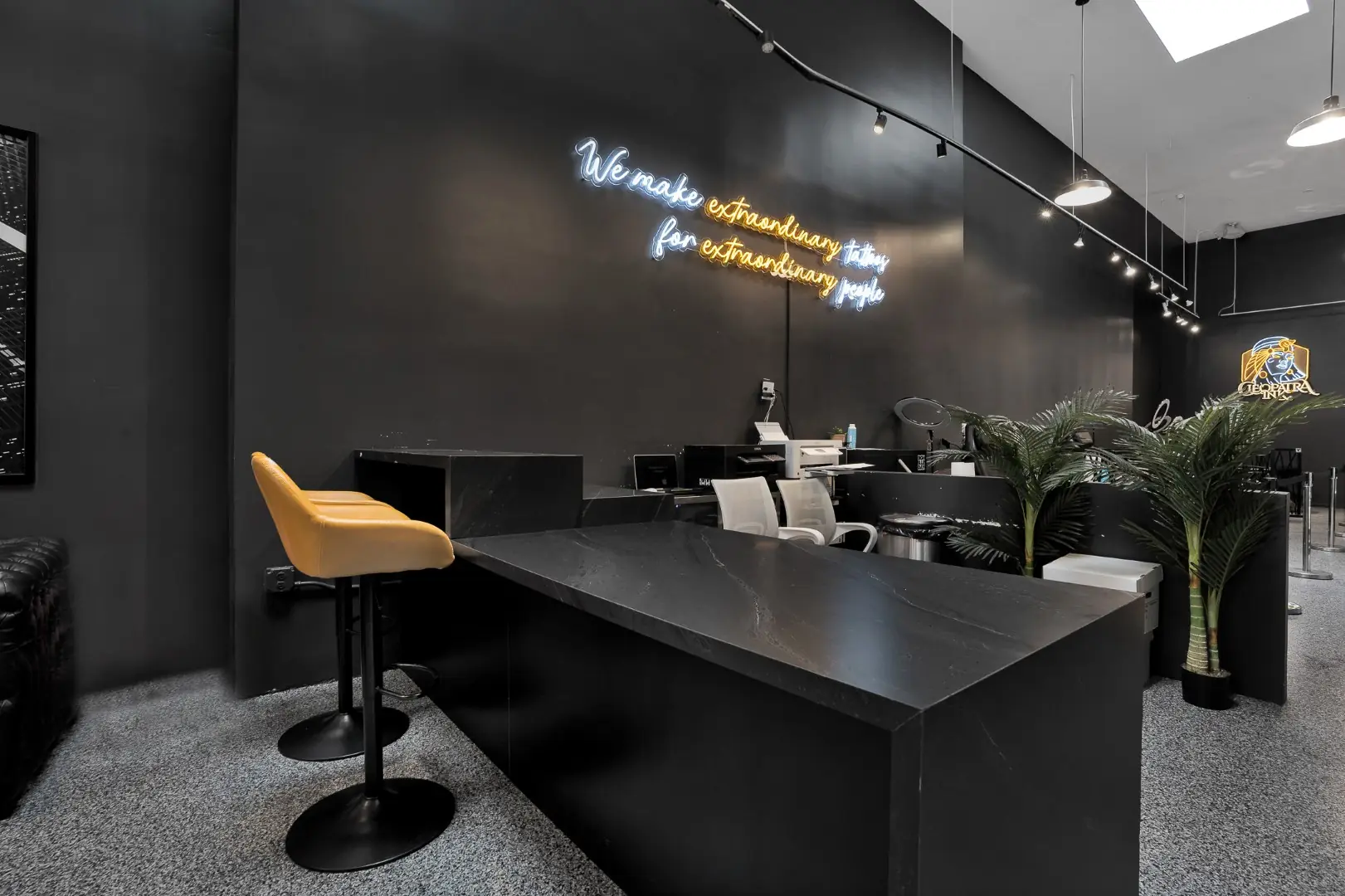 Cleopatra Tattoo consultation table with a mustard stool and palms beneath track lighting in Santa Monica