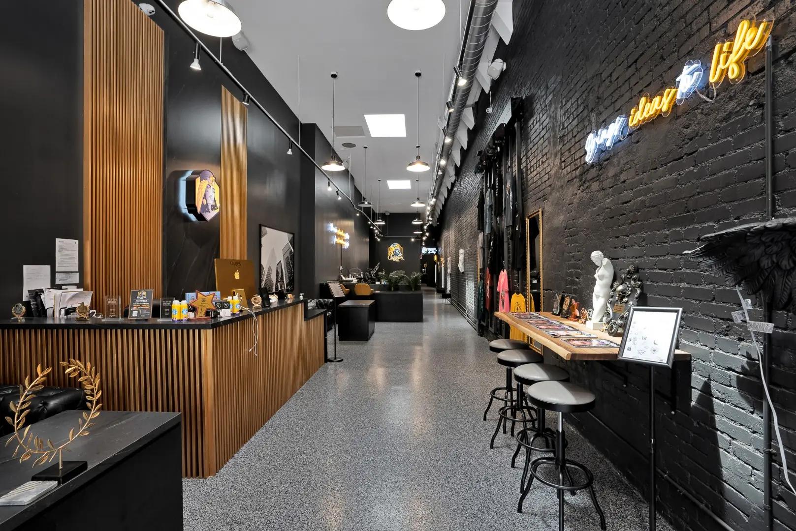 Cleopatra Tattoo studio in Santa Monica with wood slat millwork, painted brick, track lighting, and terrazzo-look flooring