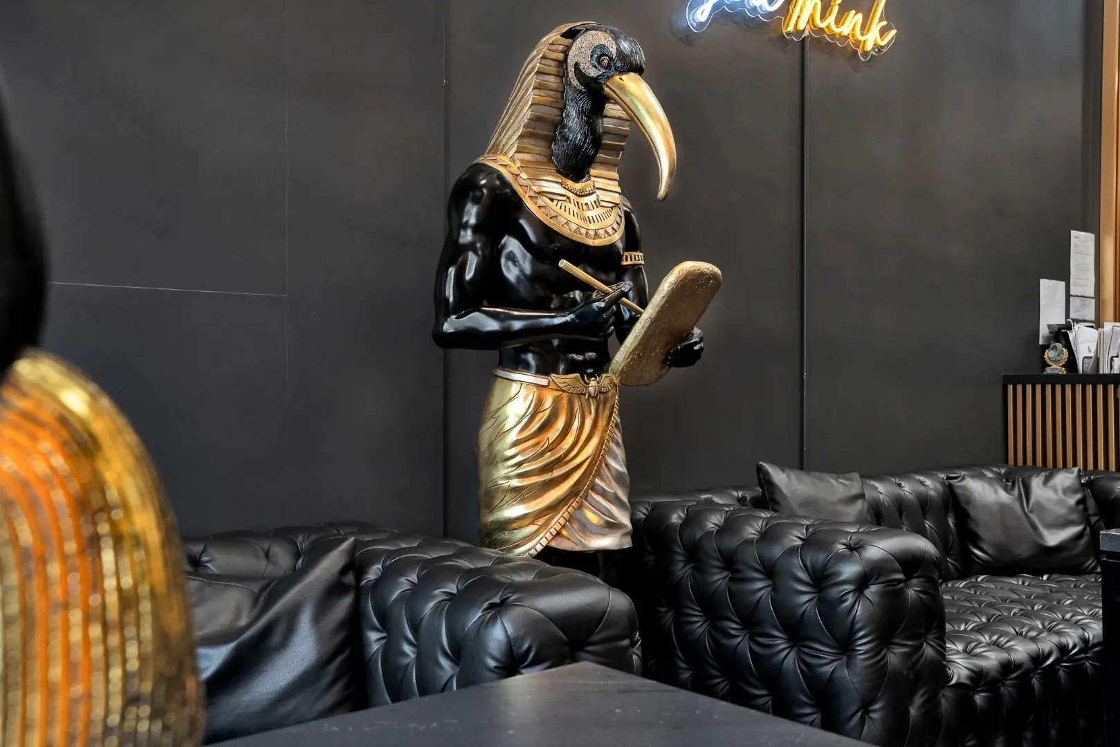 Cleopatra Tattoo lounge with a gold Egyptian statue and tufted black leather sofas in Santa Monica
