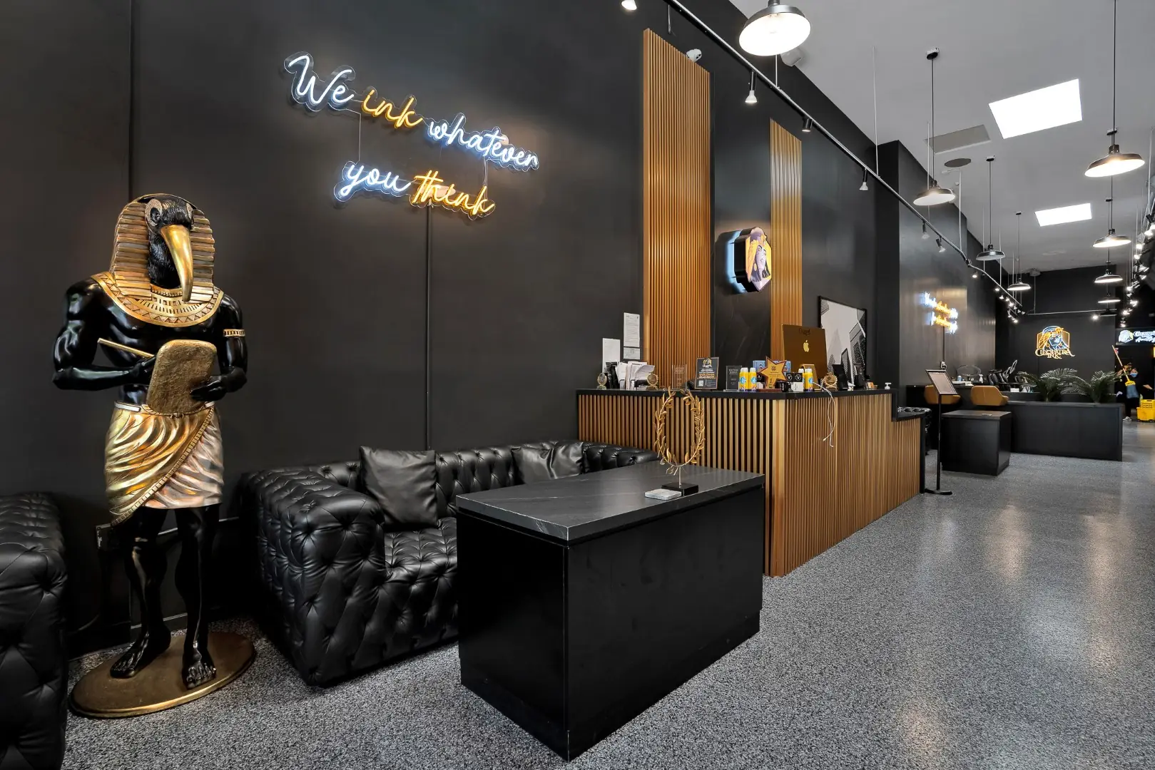Cleopatra Tattoo lounge with tufted leather seating, a gold Egyptian statue, and a neon sign leading to reception in Santa Monica
