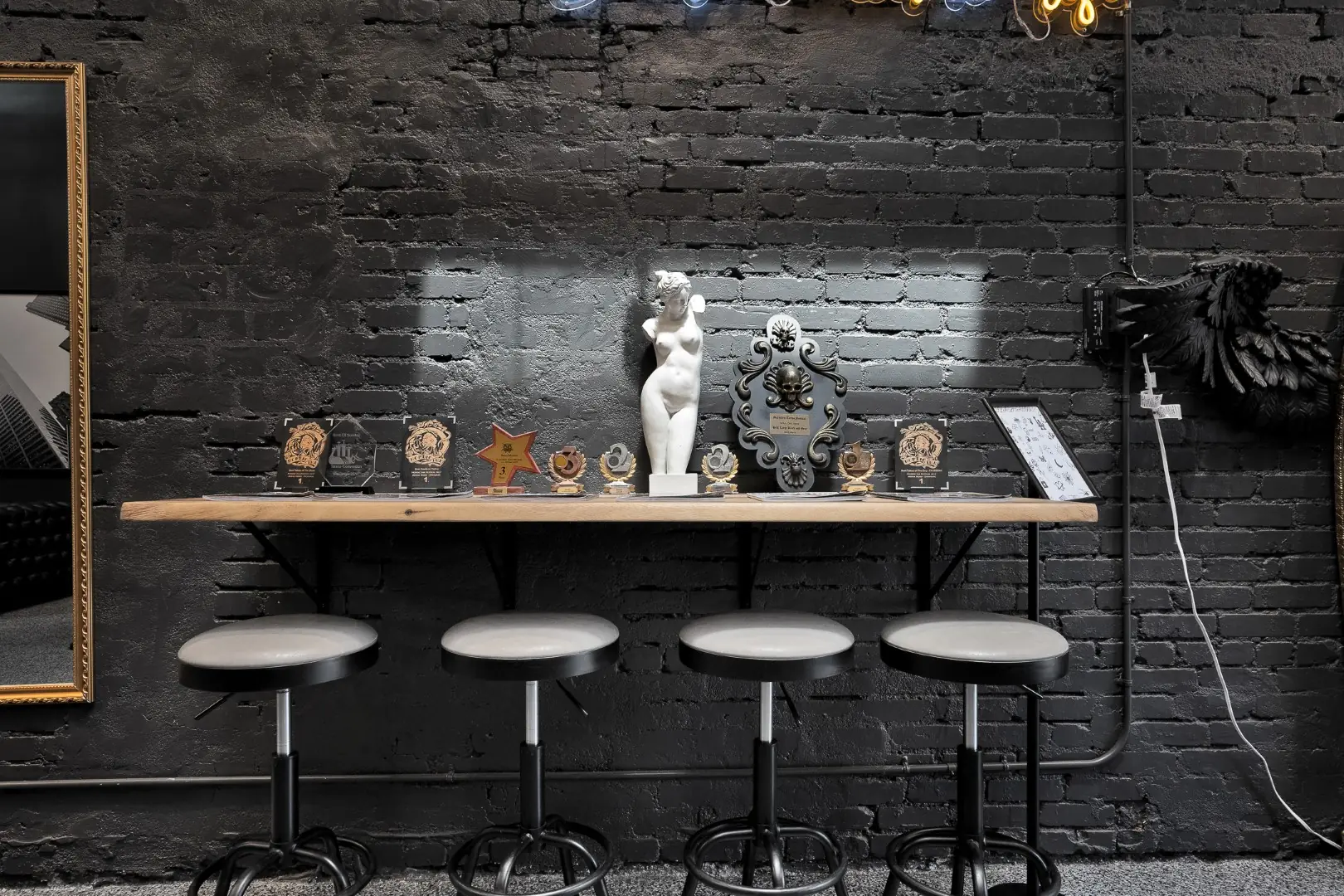 Cleopatra Tattoo bar counter with metal stools against a painted black brick wall in Santa Monica