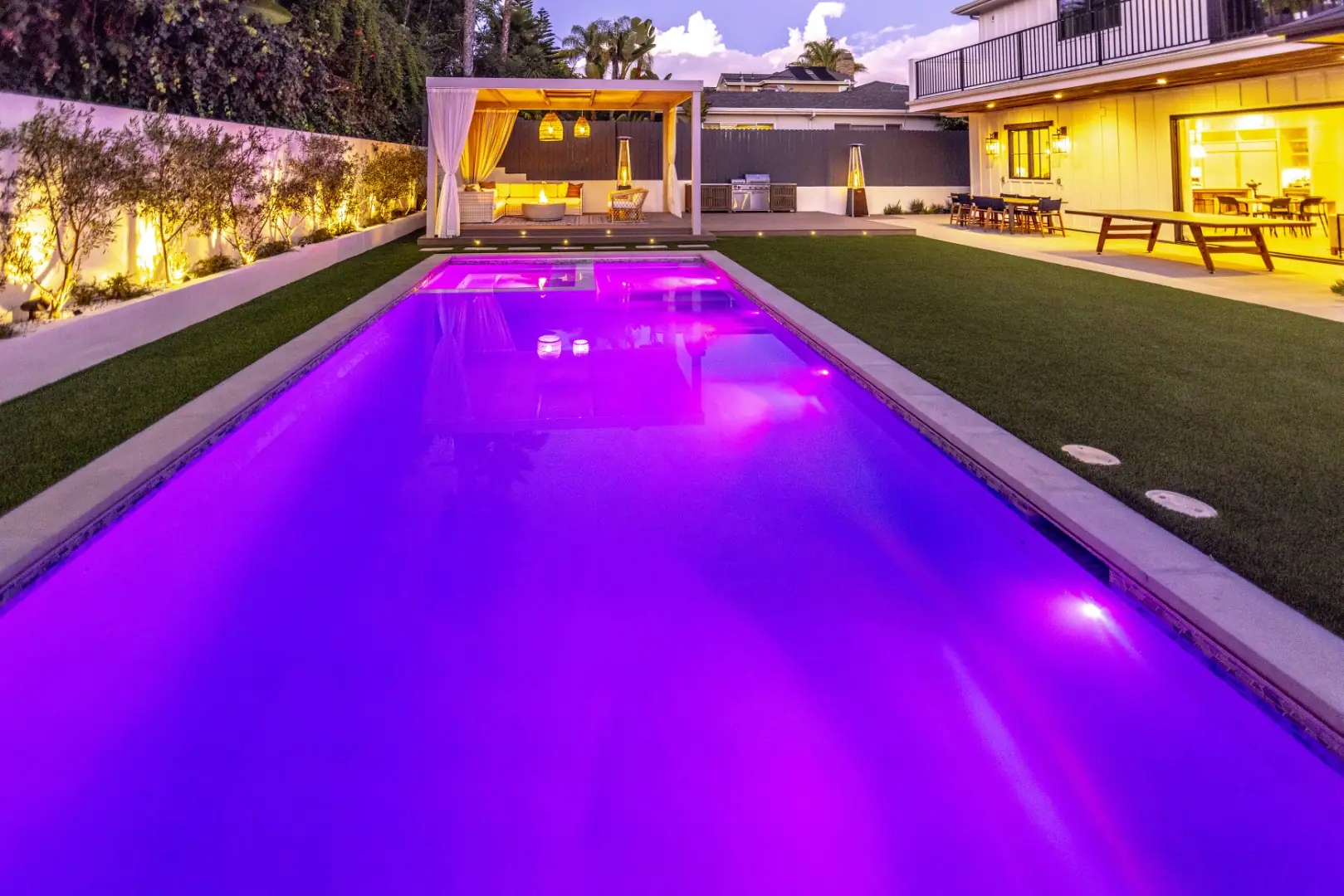 Sheens Project pool lit magenta with color-changing LED lights, with the cabana and outdoor kitchen behind, in Los Angeles