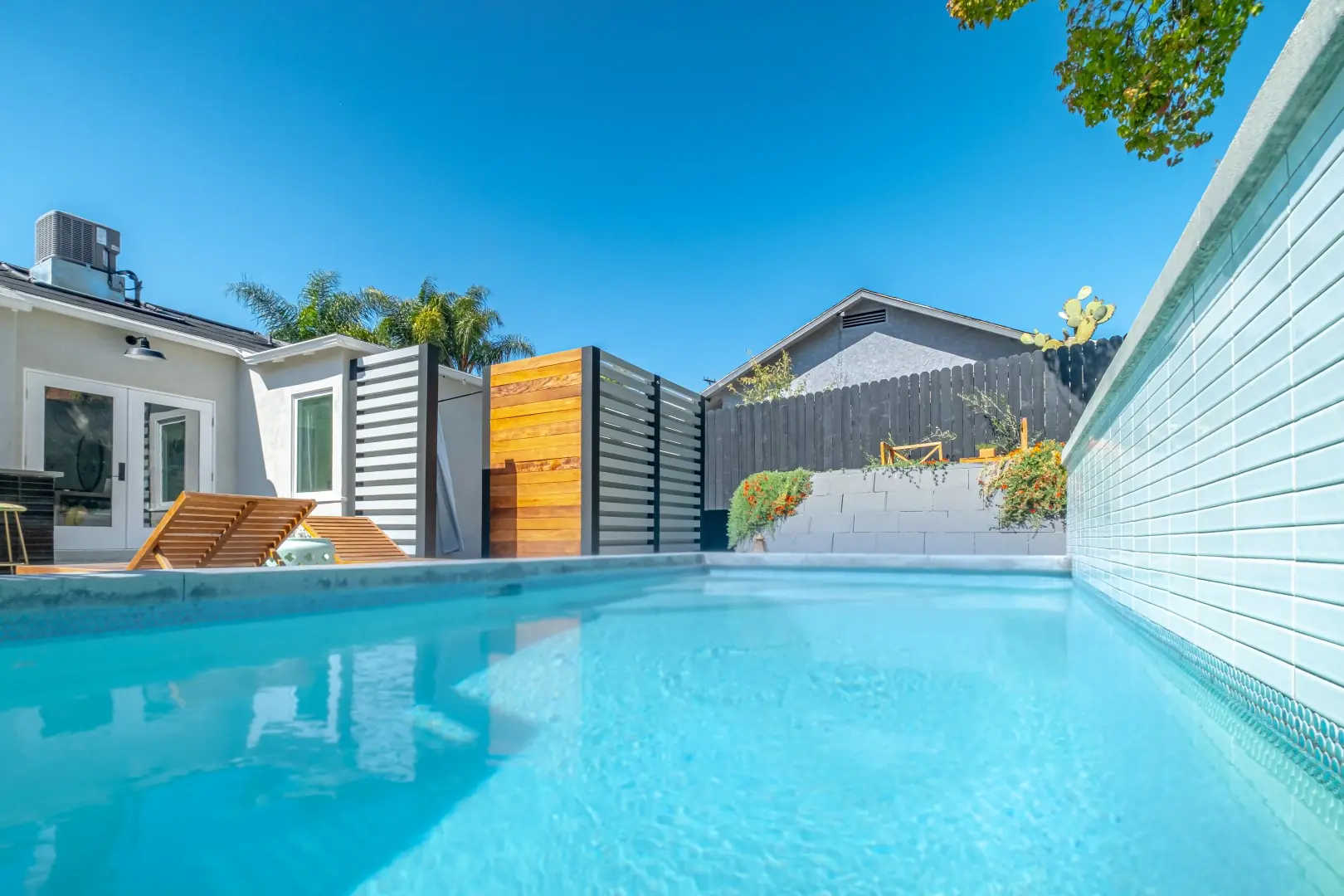 Custom pool with a raised glass-tile wall beside a modern home and slat privacy screens in Los Feliz