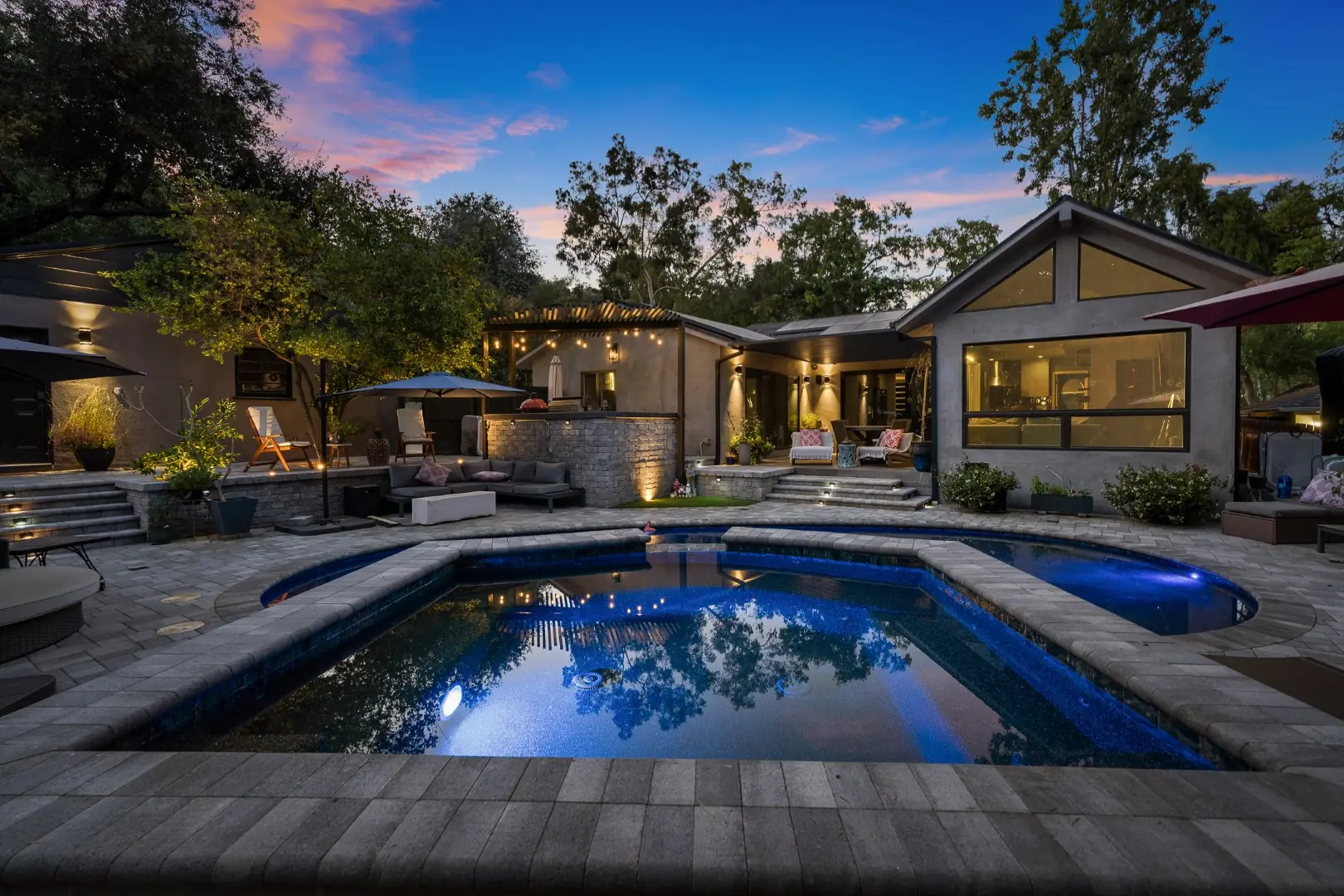 Freeform pool with a raised spa at dusk facing a modern gabled home in Pasadena