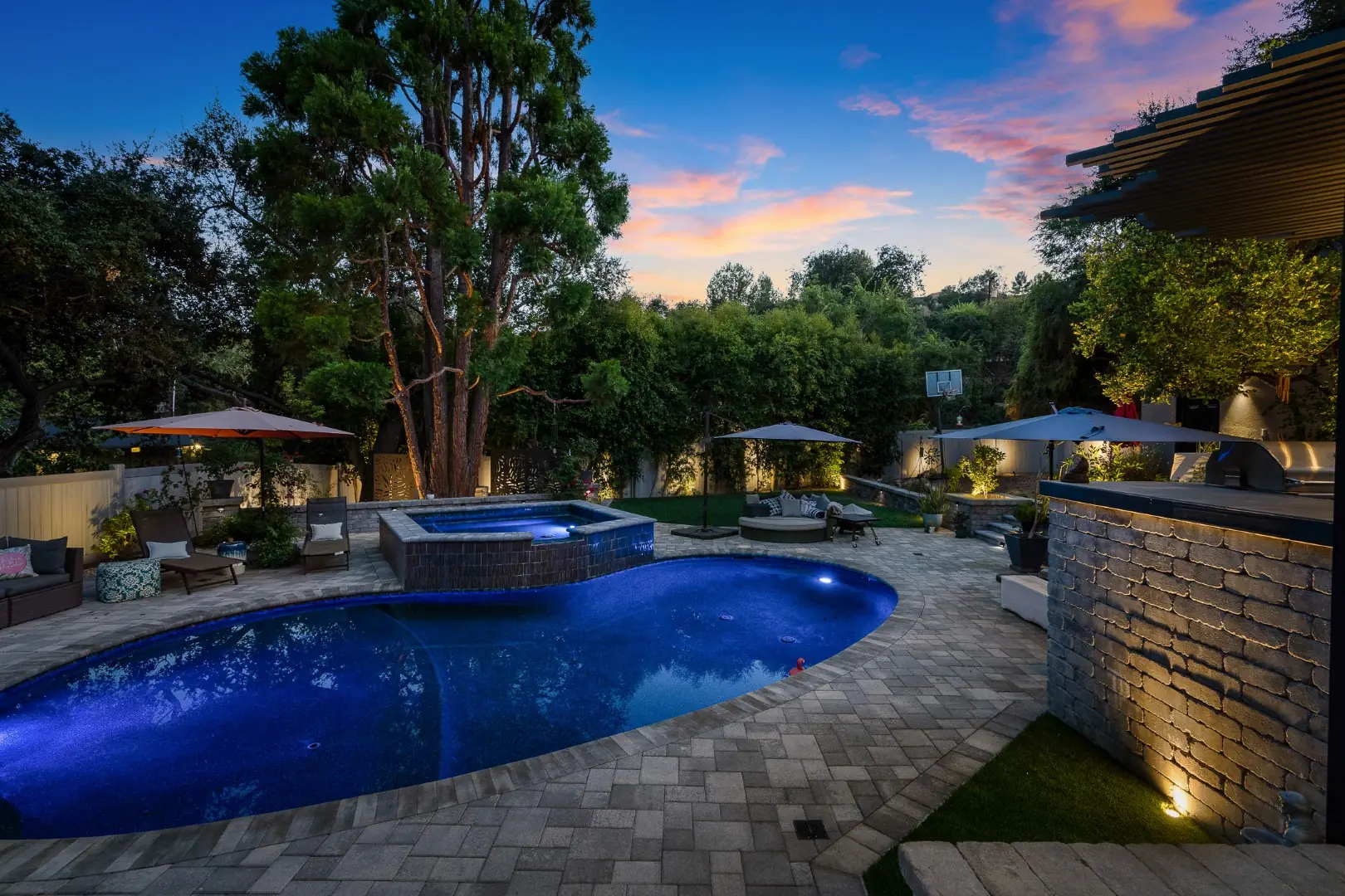 Pool and raised spa beside an uplit outdoor kitchen island at dusk in Pasadena