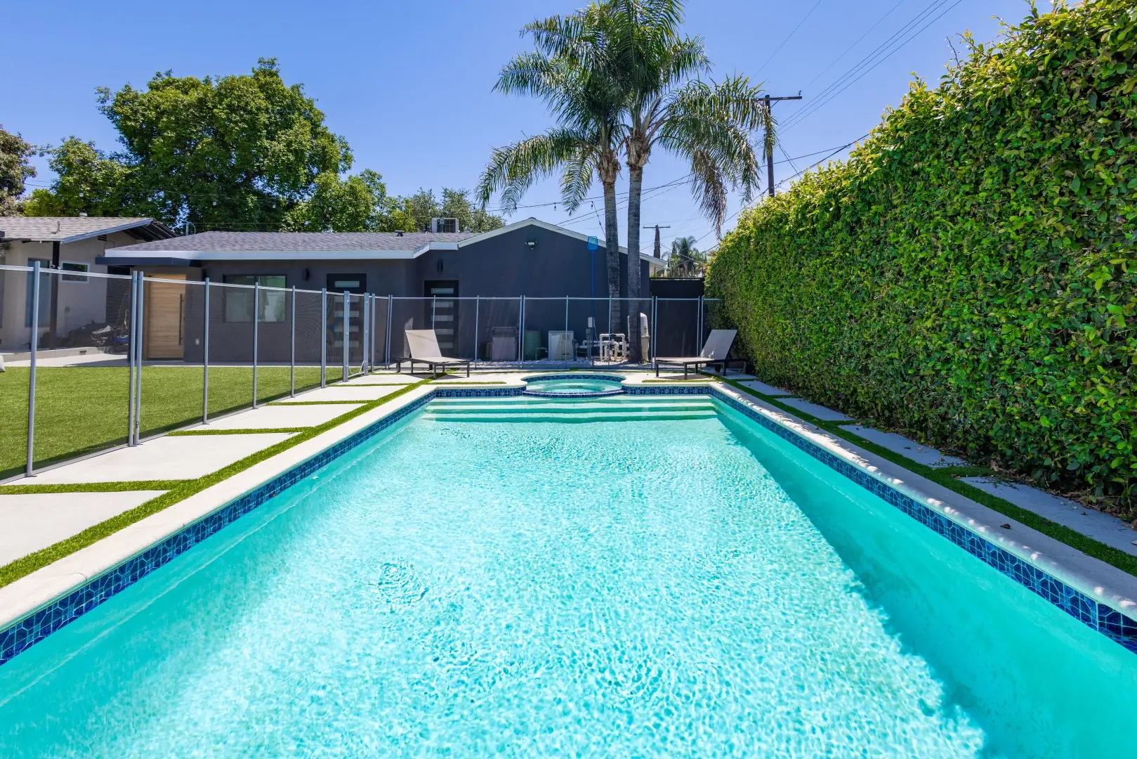 Pool with a blue tile waterline, a tall privacy hedge, and a safety fence in Reseda, Los Angeles