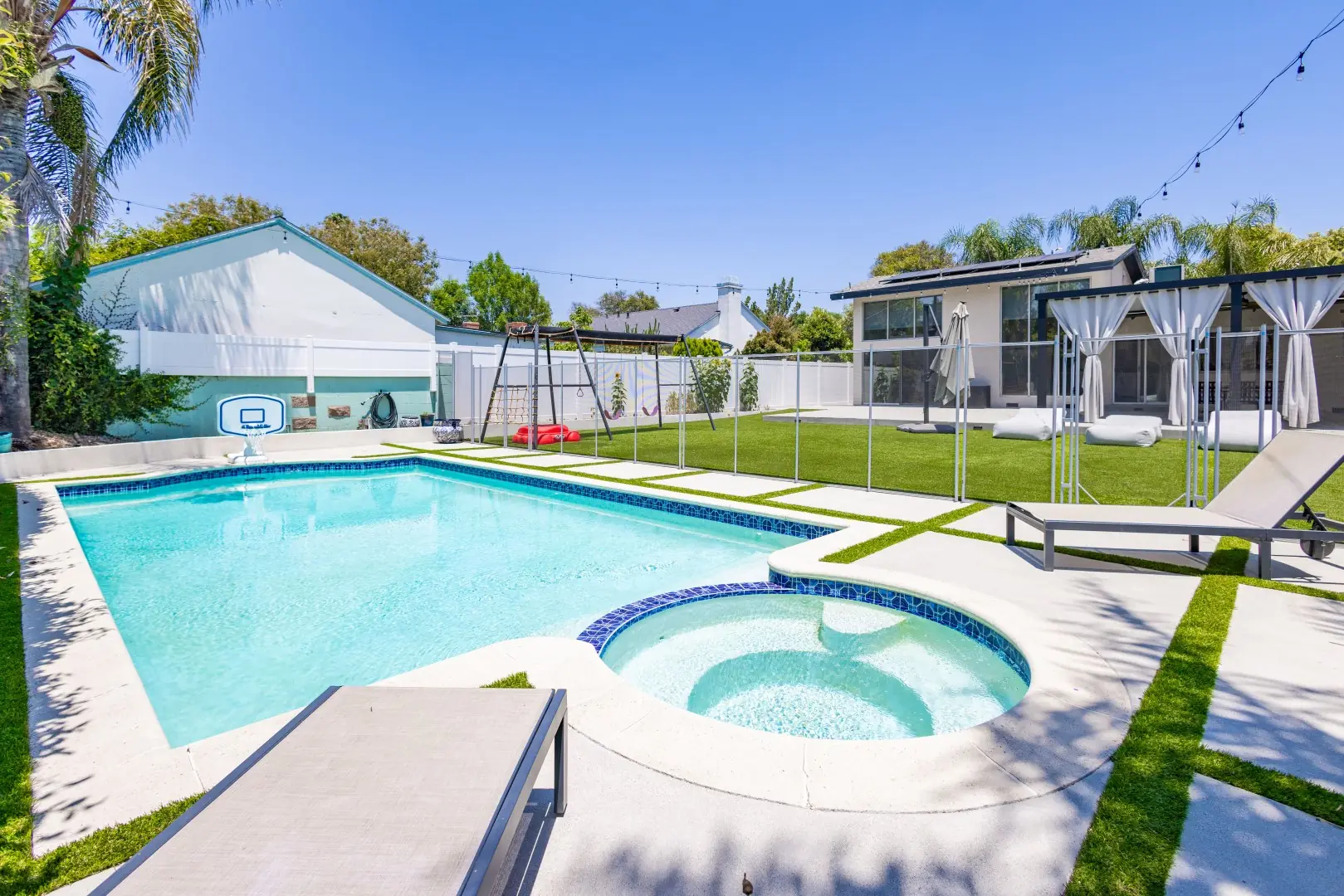 Rectangular pool with a round spa and blue tile waterline beside turf and concrete pavers in Reseda, Los Angeles