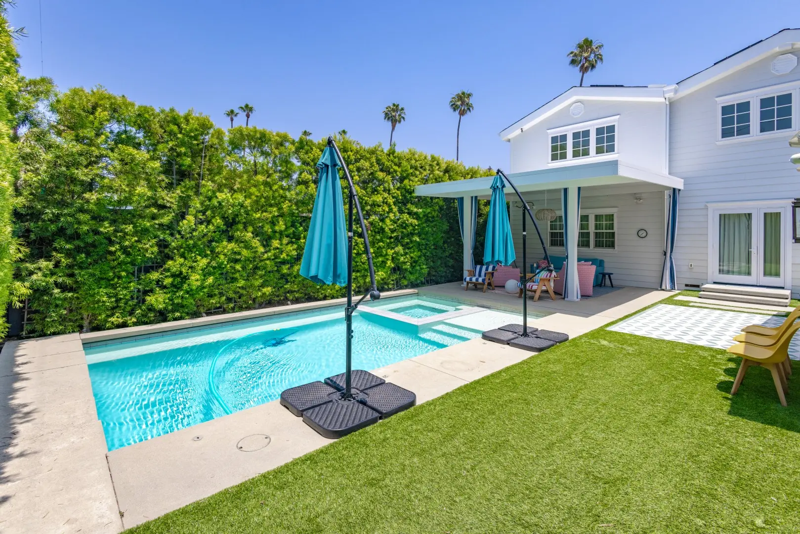 Pool with an attached spa, turf lawn, and a white patio cover with striped curtains at a Studio City home
