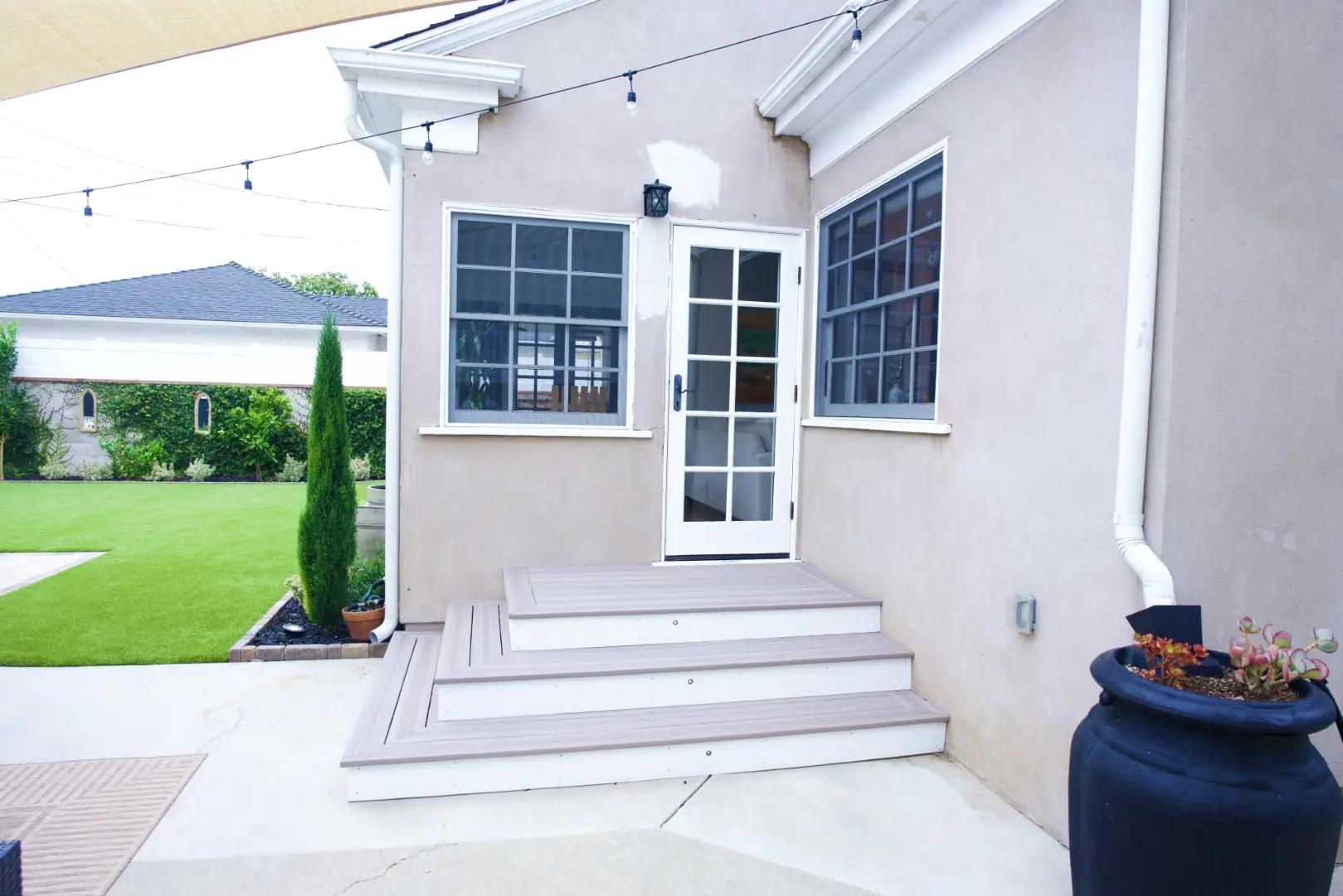 Agnew Project wide composite steps leading to a French door at the back of a Los Angeles home, with string lights overhead