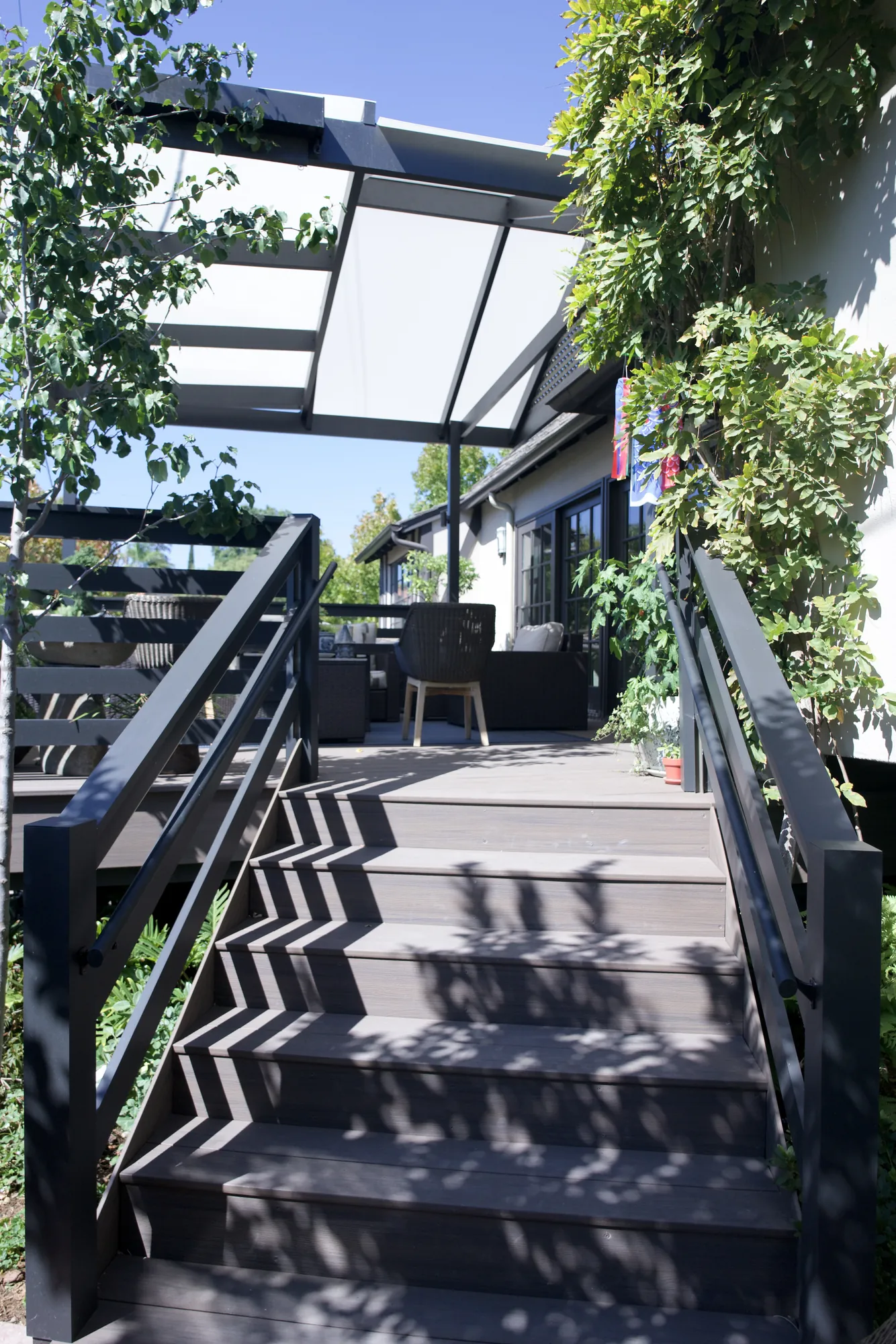 Composite stairs with dark metal rails leading up to a pergola-covered deck in Los Angeles