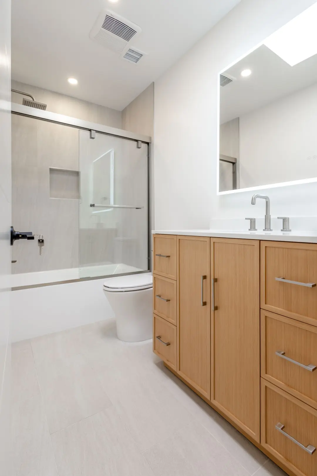 Bathroom with a wood vanity, LED mirror, and glass tub-shower enclosure in a Northridge renovation