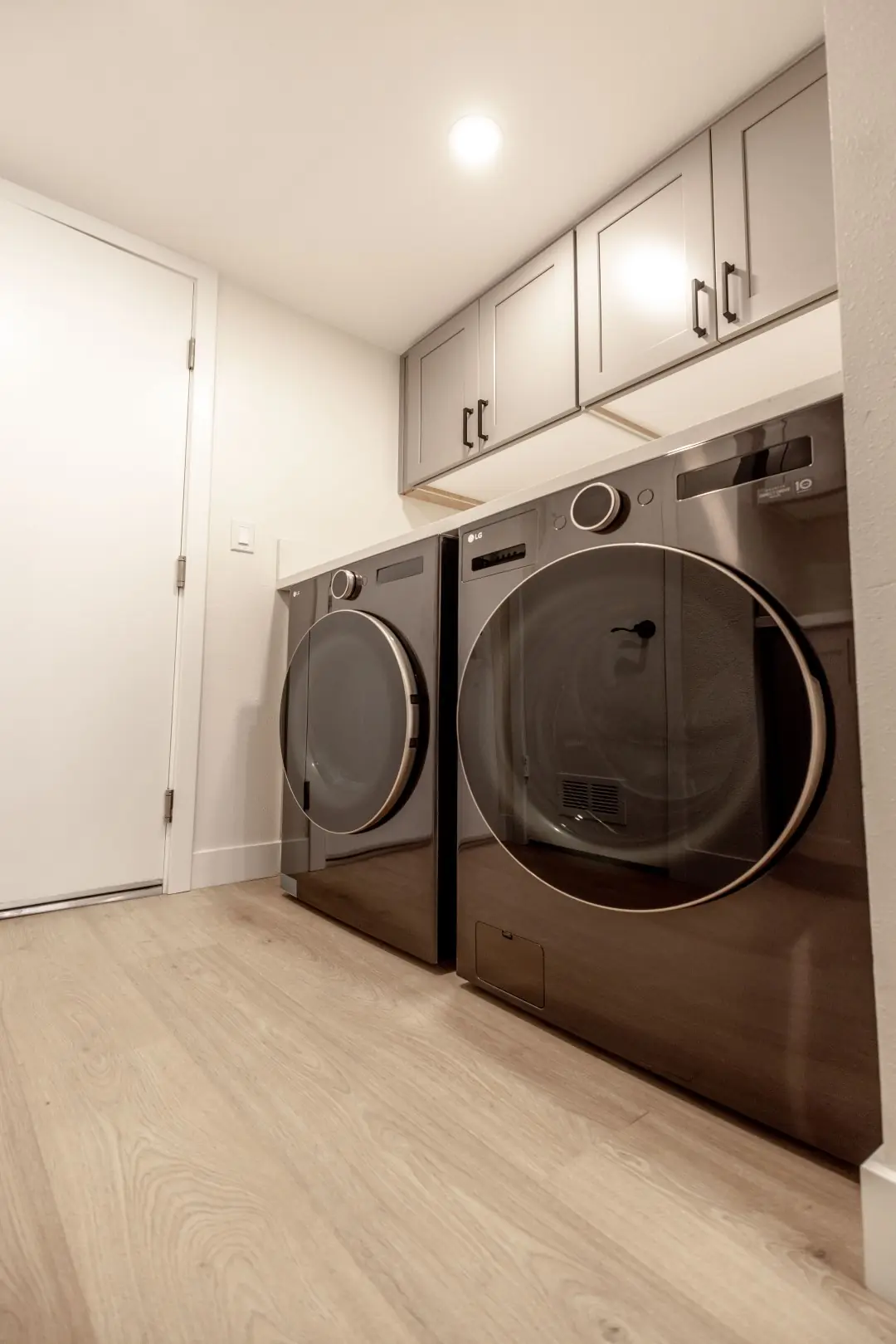Laundry room with a front-load washer and dryer under gray cabinets in a Northridge renovation