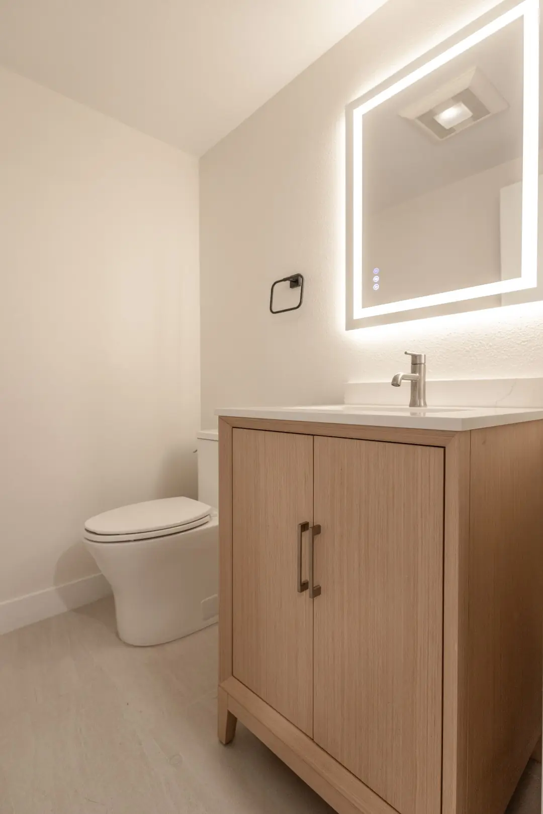 Powder room with a light wood vanity and backlit mirror in a Northridge full-home renovation
