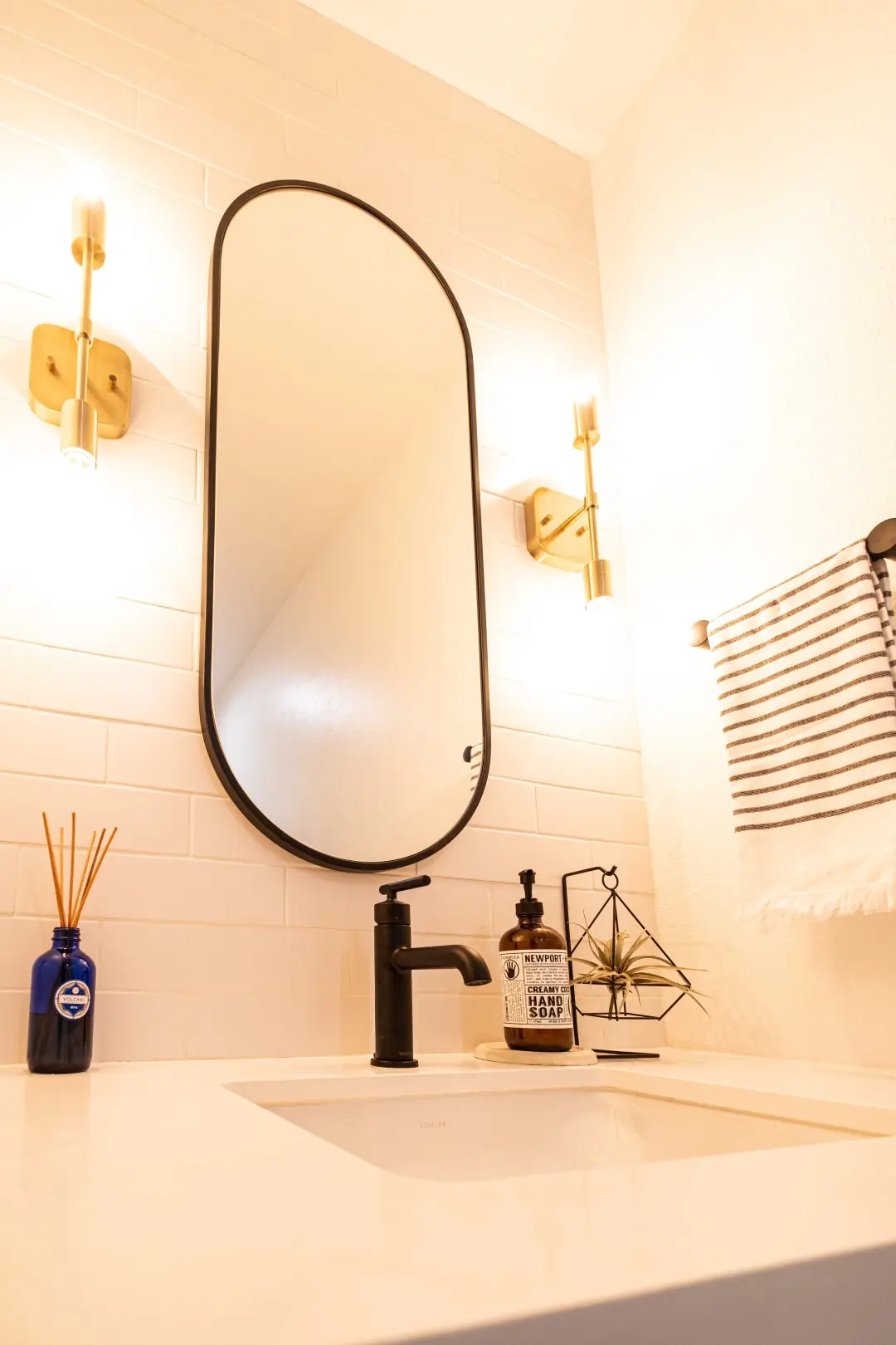 Powder room vanity with a matte black faucet, oval mirror, and brass sconces in a West LA renovation