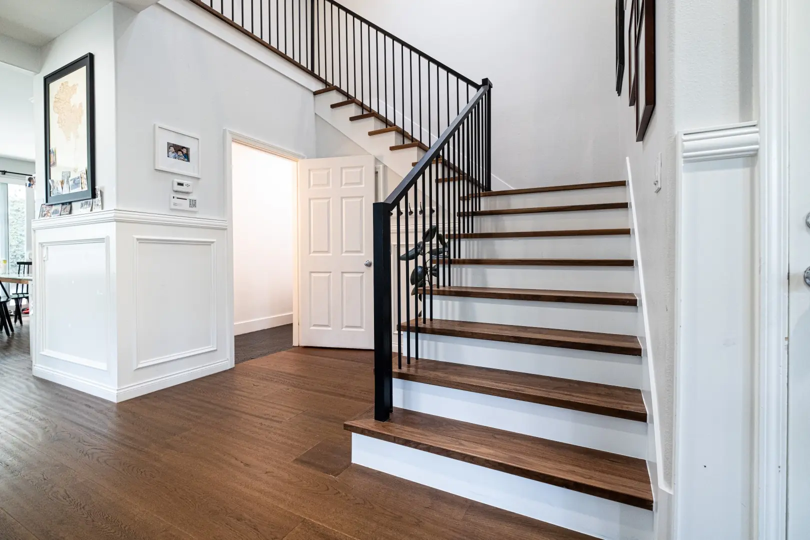 Renovated staircase in a West LA home with black iron balusters, walnut-stained treads, and white risers beside wainscoted walls