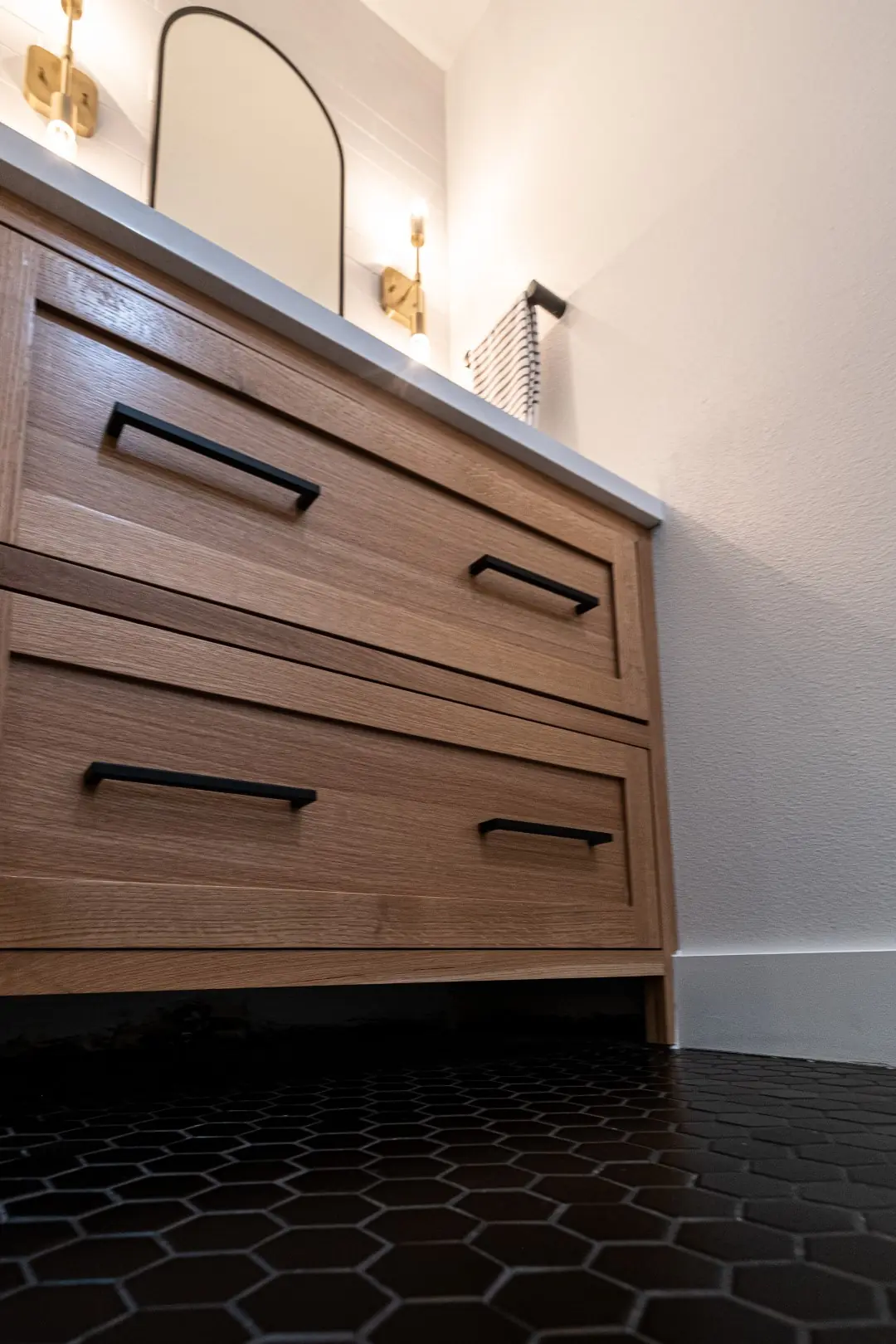 Walnut vanity drawers with black pulls over black hexagon tile in a West LA powder room