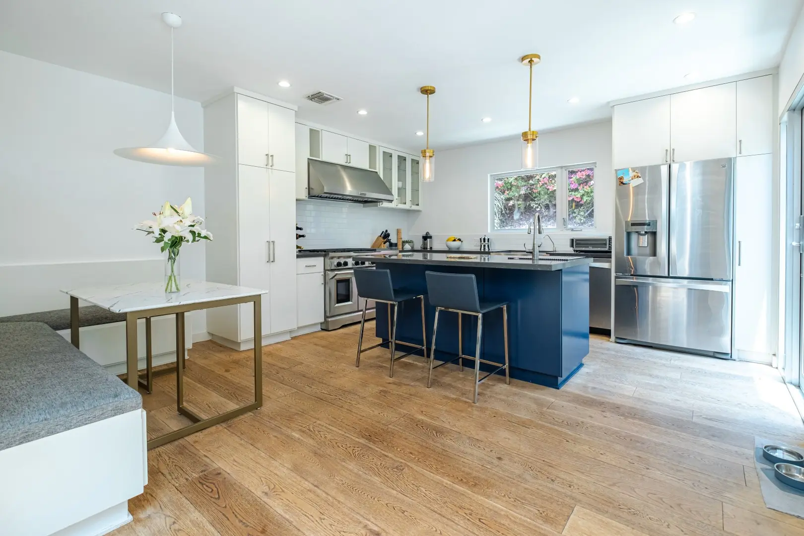 Kitchen remodel in Santa Monica with a navy island, white cabinetry, brass pendants, and a built-in breakfast nook