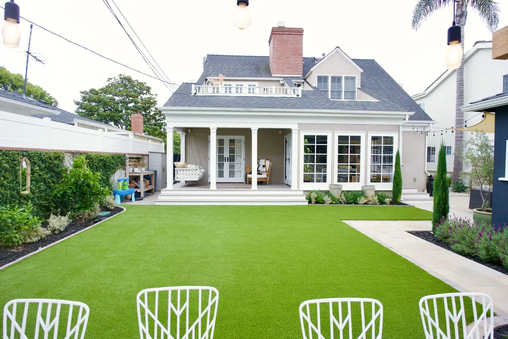 Backyard artificial turf lawn with planted borders and a paver walkway leading to a covered back porch in Los Angeles