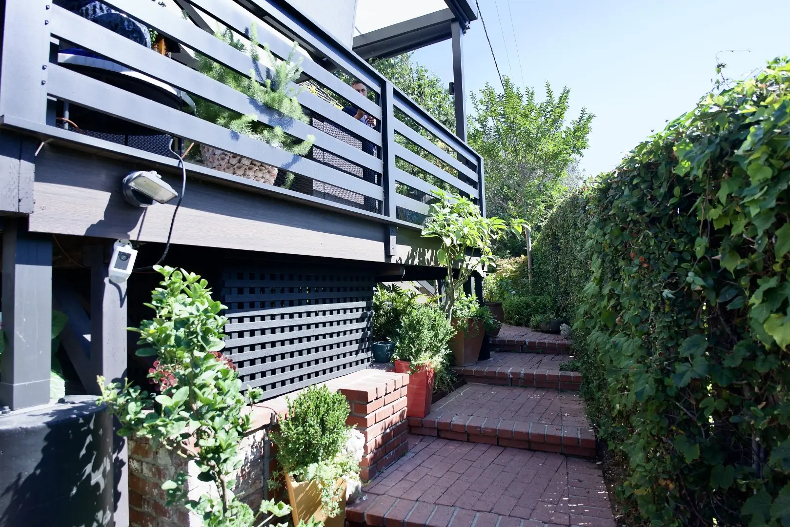 Red brick garden steps climbing a narrow side yard beside an ivy-covered wall and a dark wood deck in Los Angeles