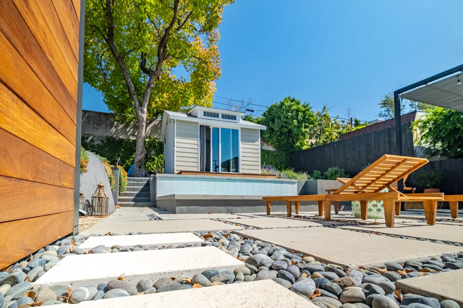 Concrete pavers set in river pebbles leading past teak lounge chairs to a backyard studio in Los Feliz