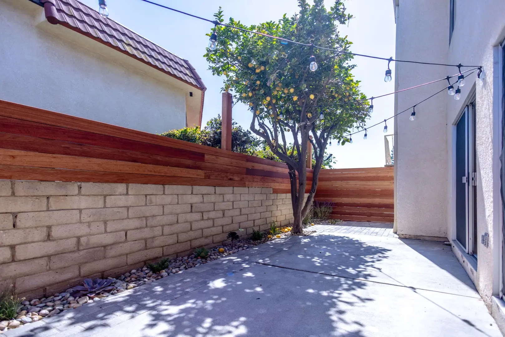 Concrete patio with a lemon tree, string lights, and a horizontal redwood fence in Northridge