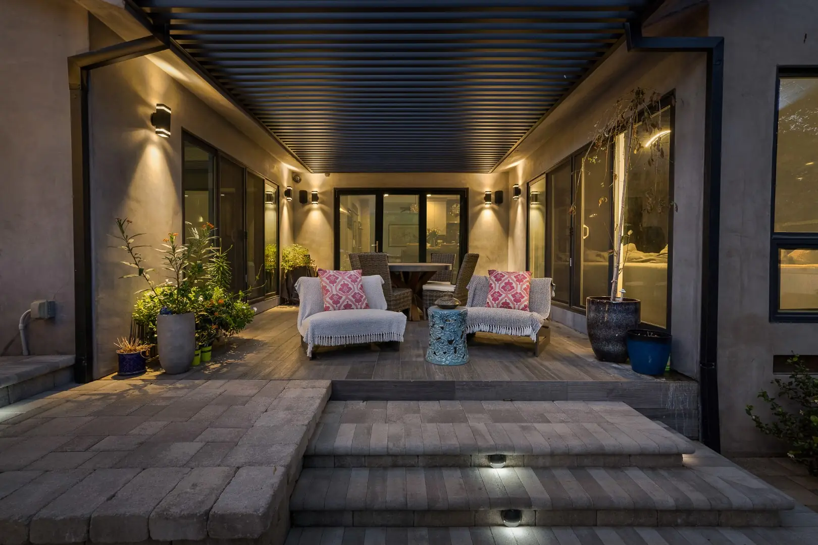 Covered patio with lounge chairs, wall sconces, and lit paver steps in Pasadena