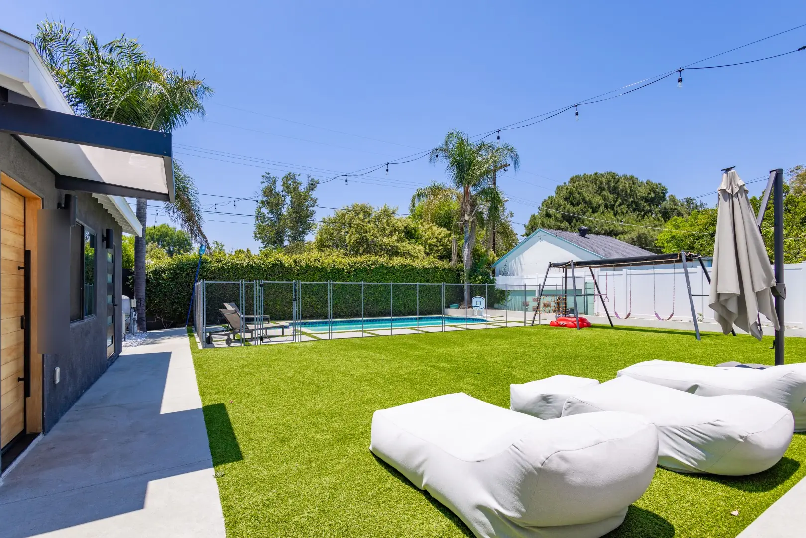 Side yard with a turf lawn, lounge cushions, and a fenced pool beyond in Reseda, Los Angeles