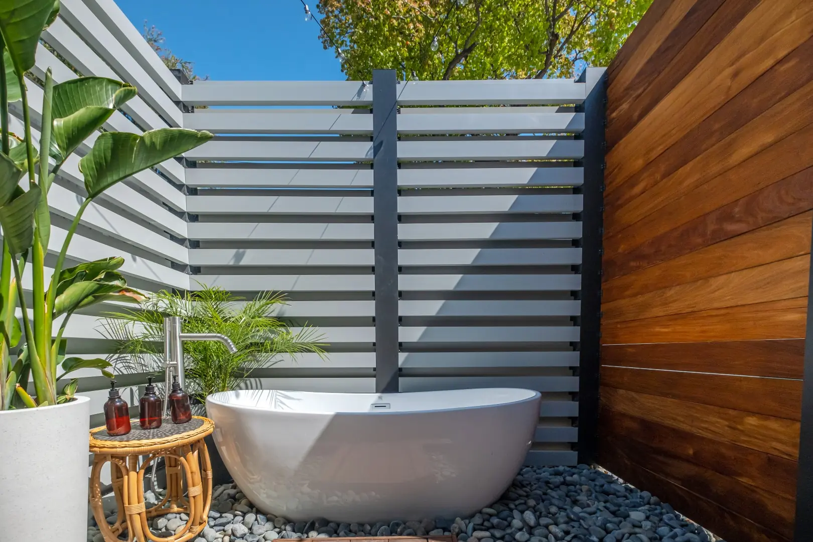 Outdoor bath in Los Feliz with a freestanding soaking tub on river pebbles, framed by a slat privacy screen and a wood panel wall
