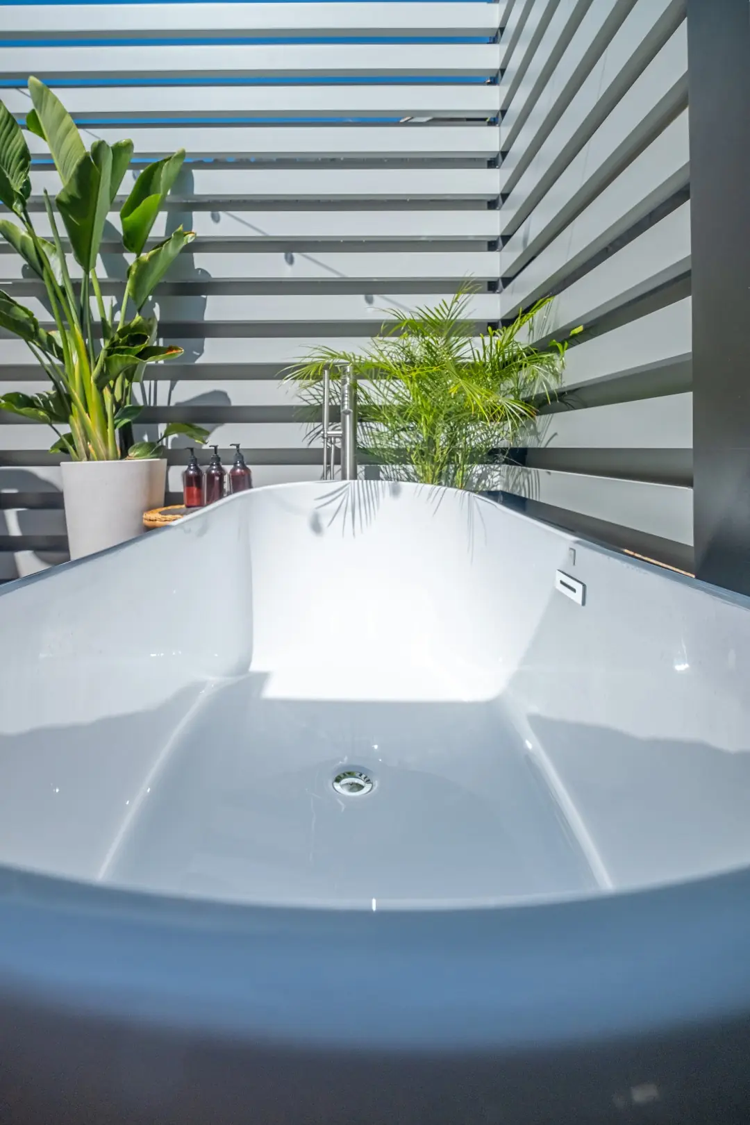 Freestanding soaking tub with tropical plants inside a slatted outdoor bath enclosure in Los Feliz