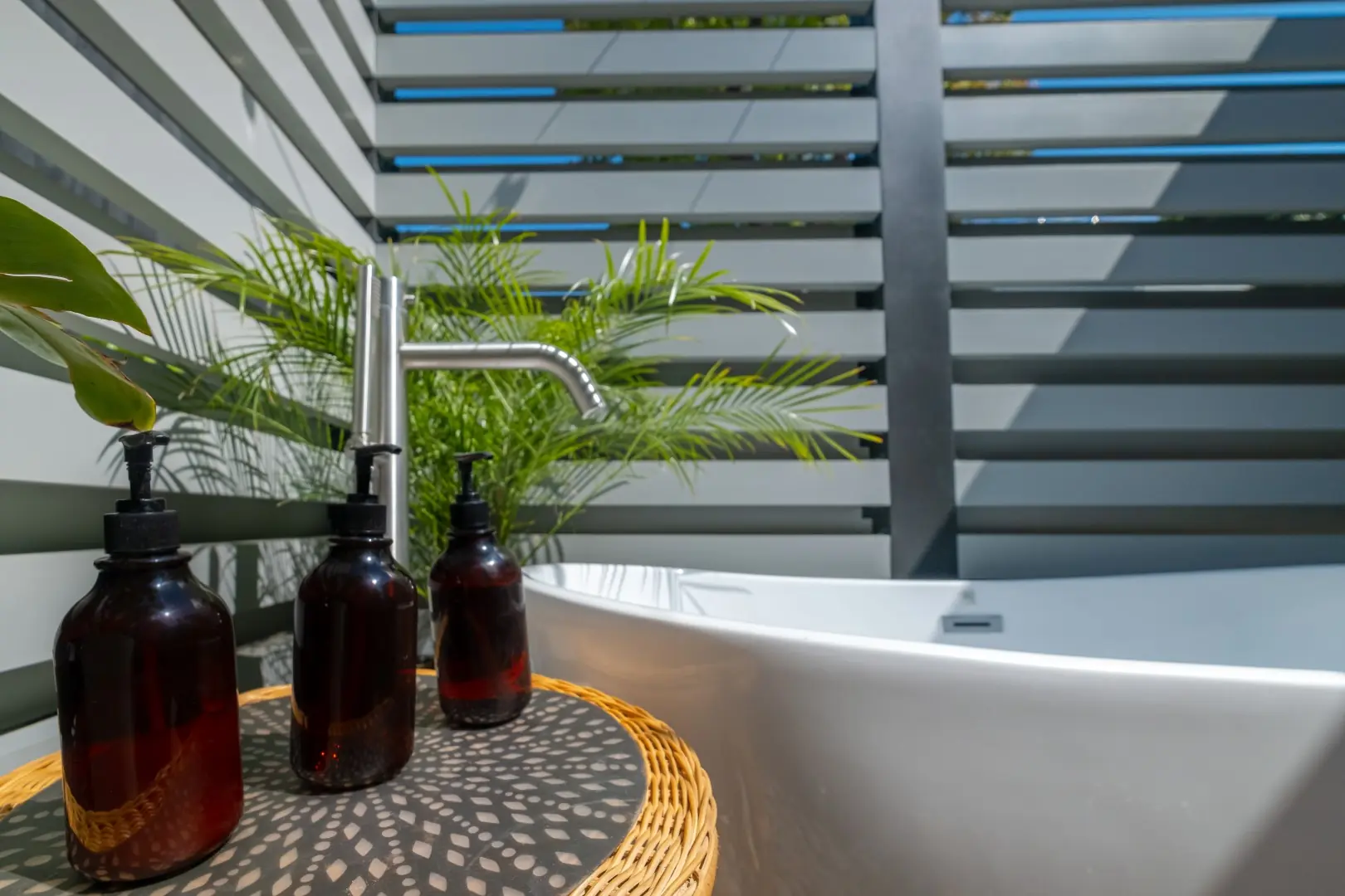 Brushed steel tub filler and amber bath bottles beside a freestanding soaking tub in an outdoor bath in Los Feliz