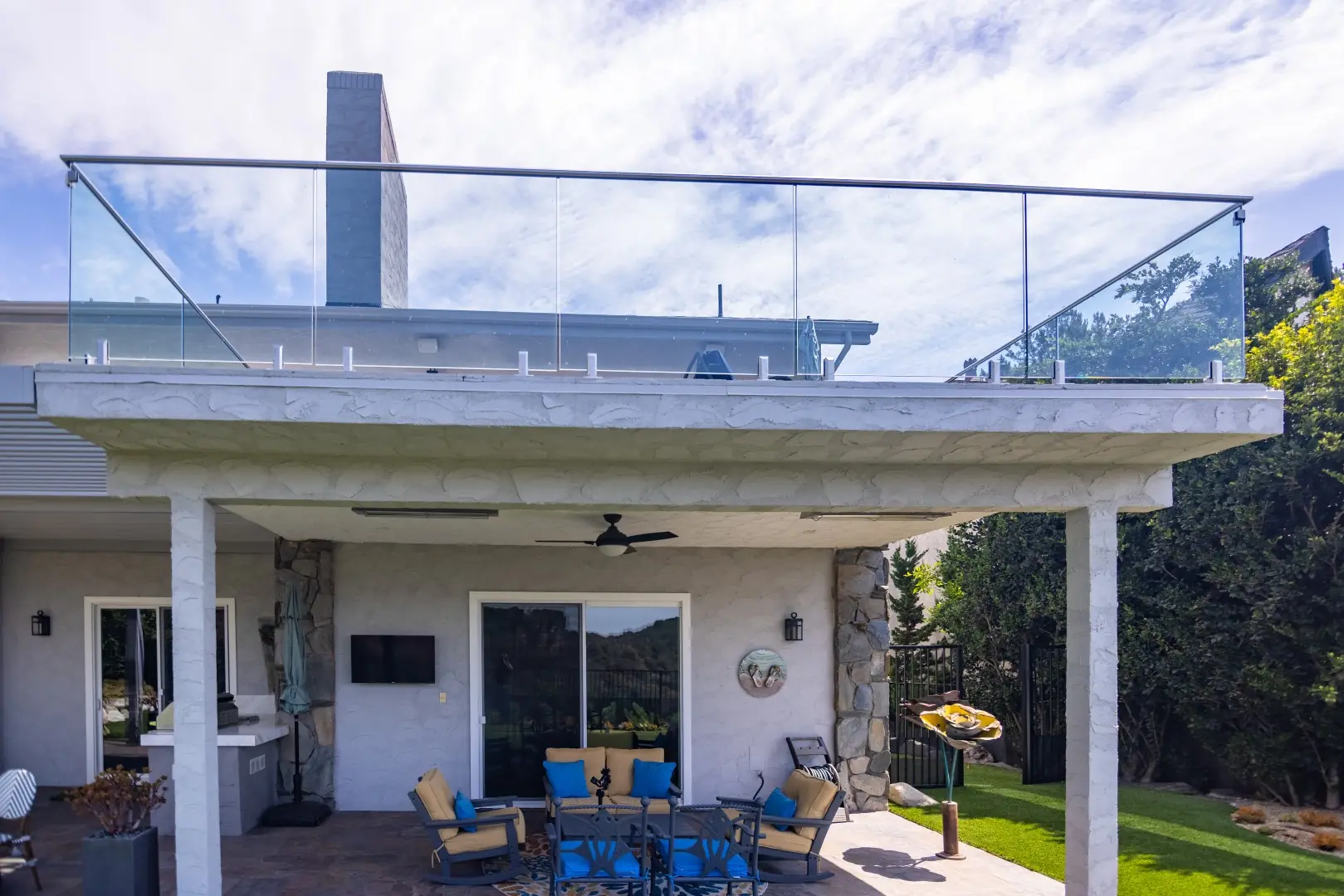 Covered patio with a ceiling fan and lounge seating beneath a glass-railed upper deck in Beverly Glen, Los Angeles