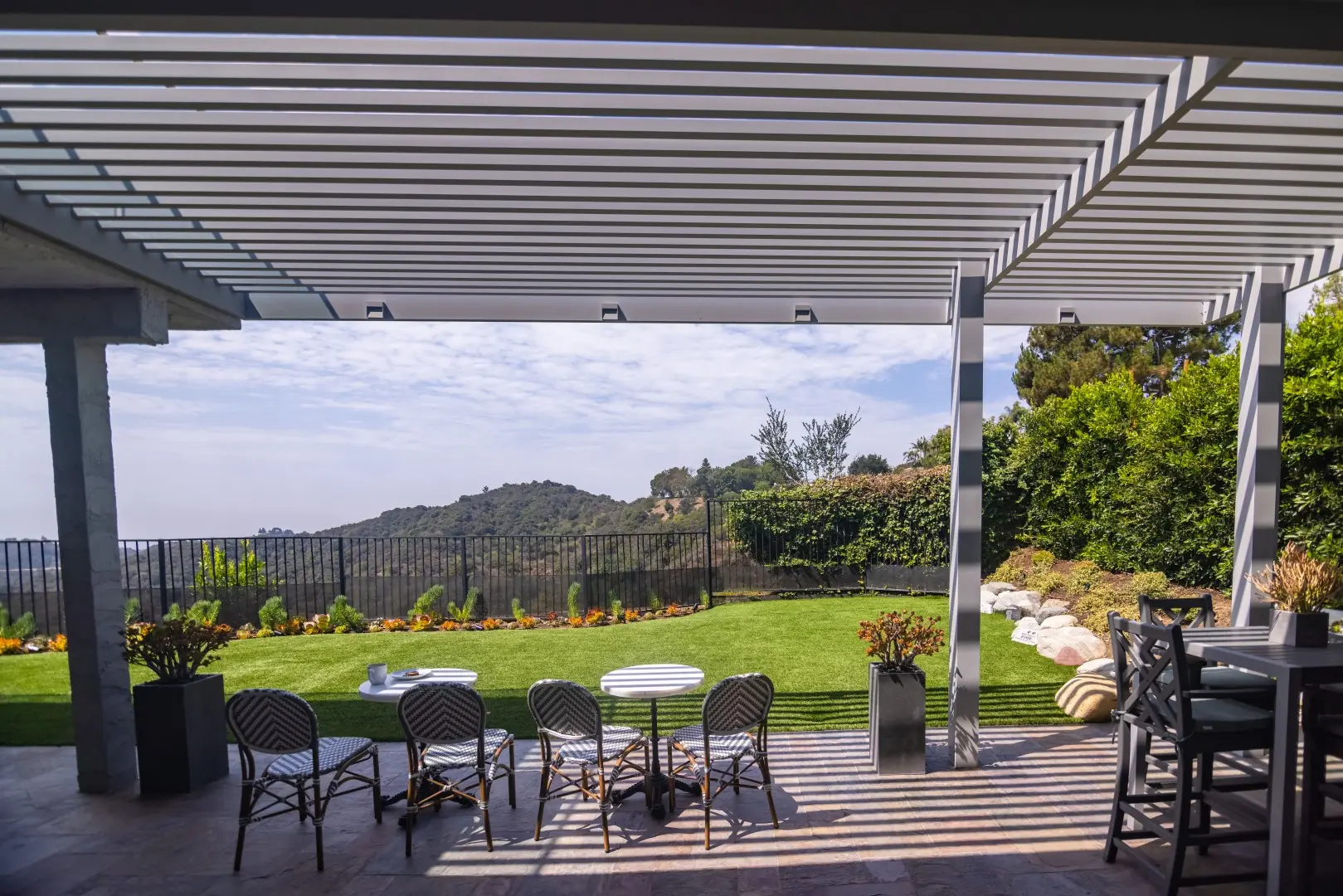 Bistro tables under a white louvered pergola facing a hillside lawn in Beverly Glen, Los Angeles