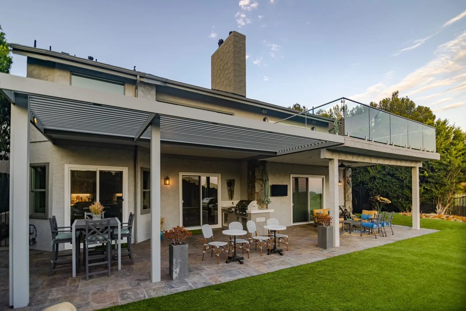 Rear of a Beverly Glen home with a louvered pergola, glass-railed balcony, and patio seating beside the lawn
