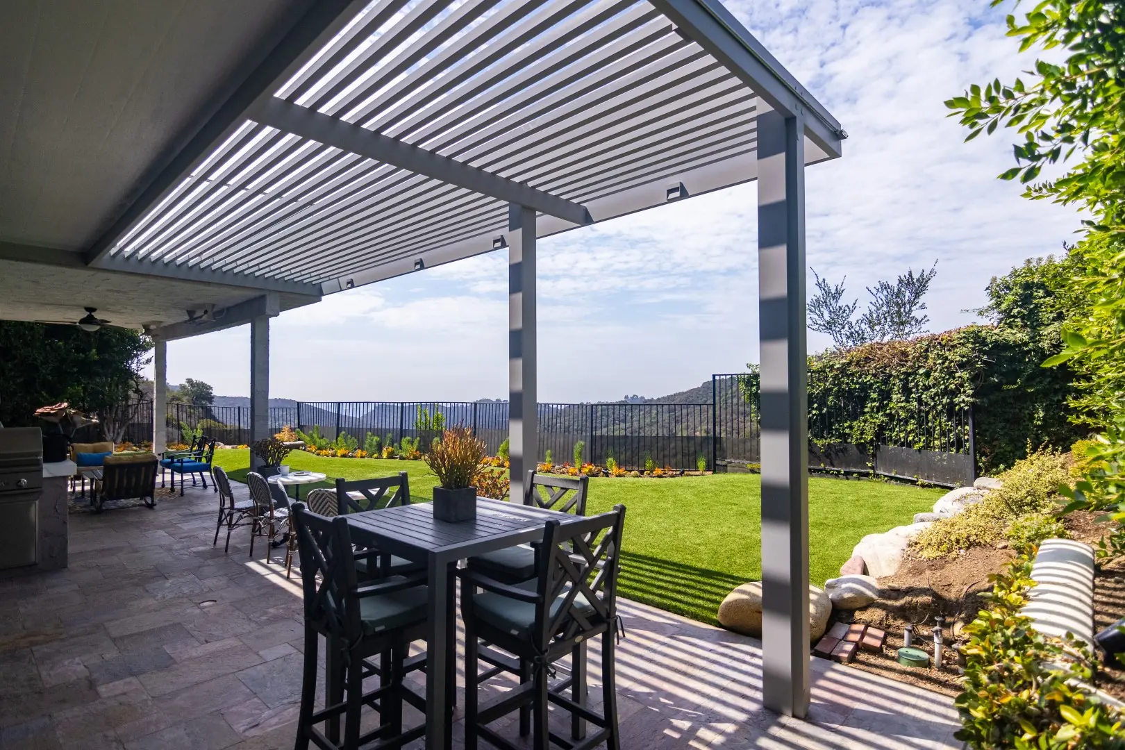 White louvered pergola shading a stone patio dining area beside a hillside lawn in Beverly Glen, Los Angeles