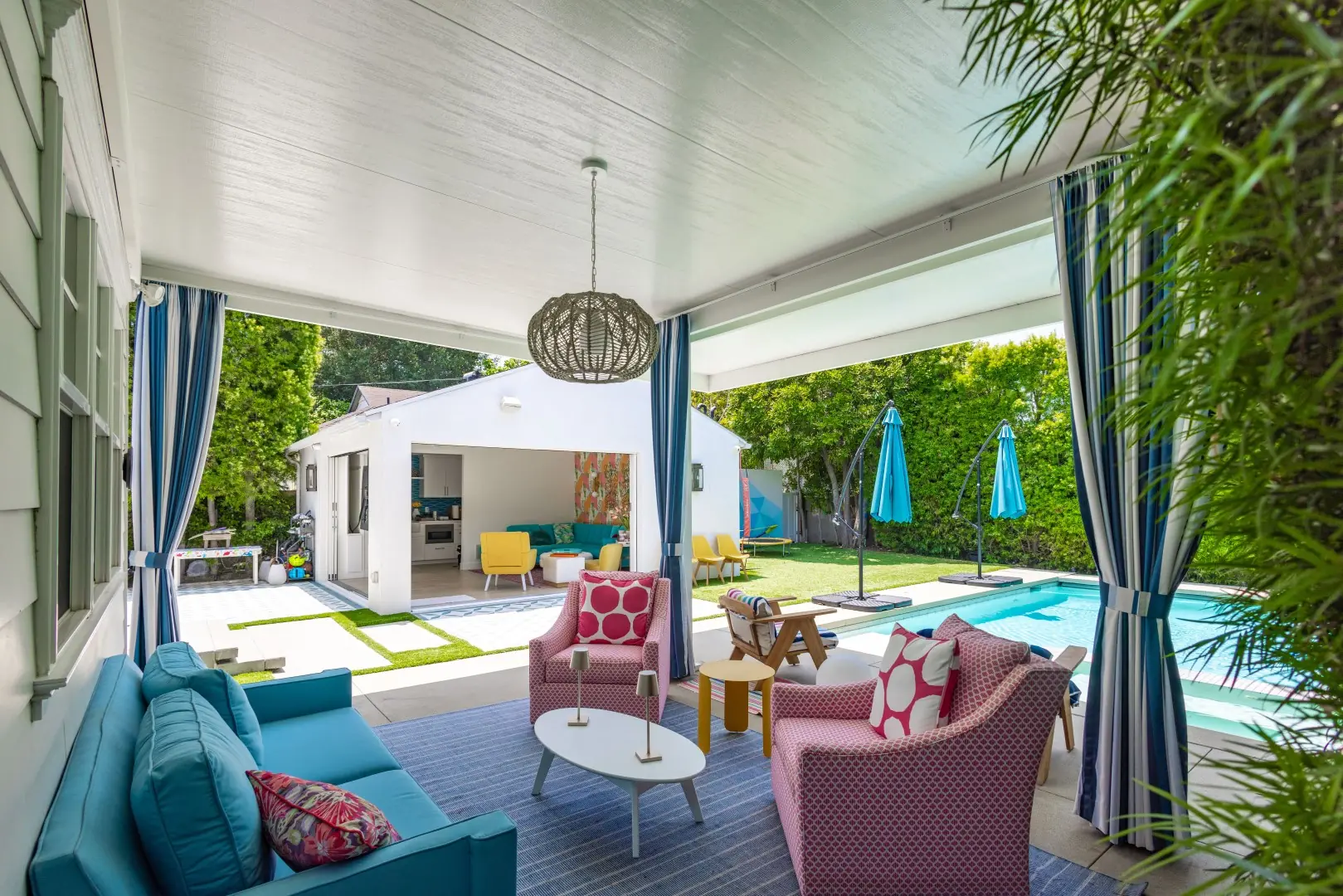 Outdoor lounge under a white patio cover with a woven pendant, facing the pool and pool house in Studio City