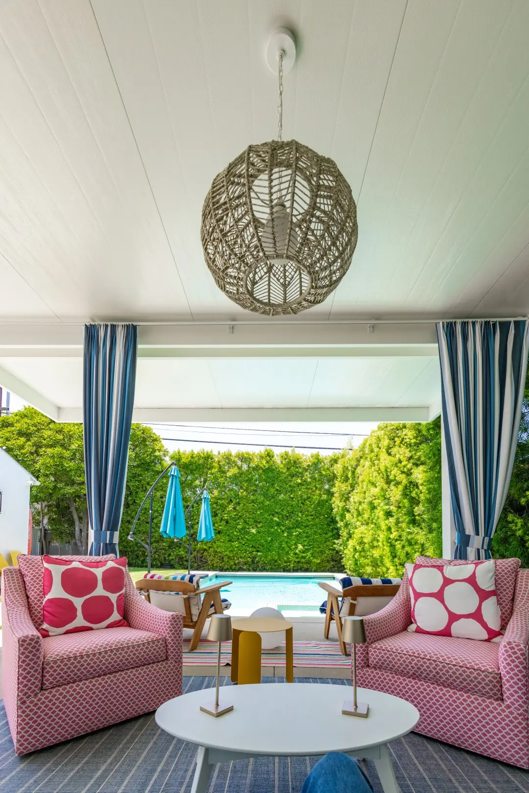 Woven pendant light above armchairs under a patio cover framed by striped curtains in Studio City