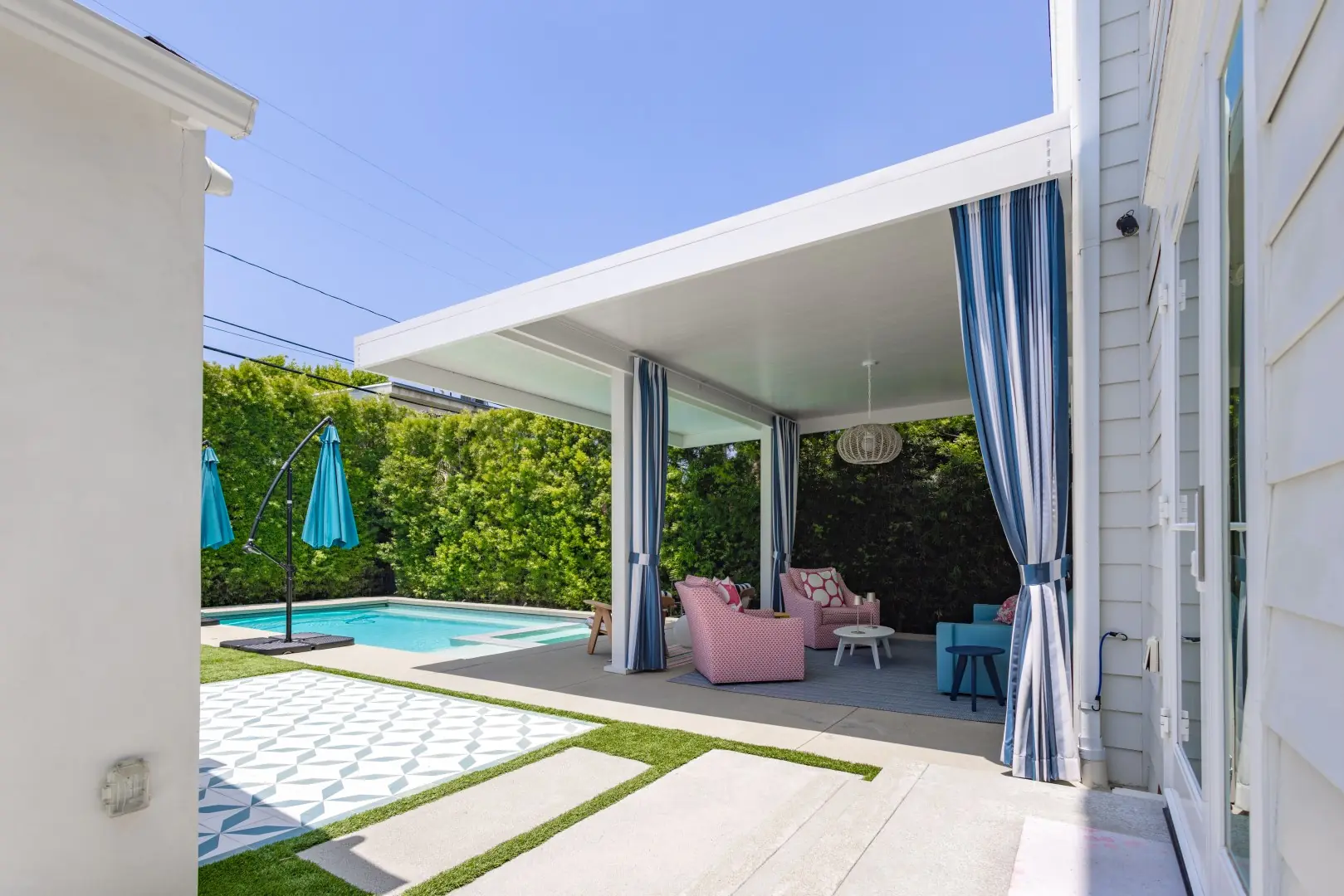Solid roof patio cover with blue striped curtains and lounge seating beside a patterned patio in Studio City