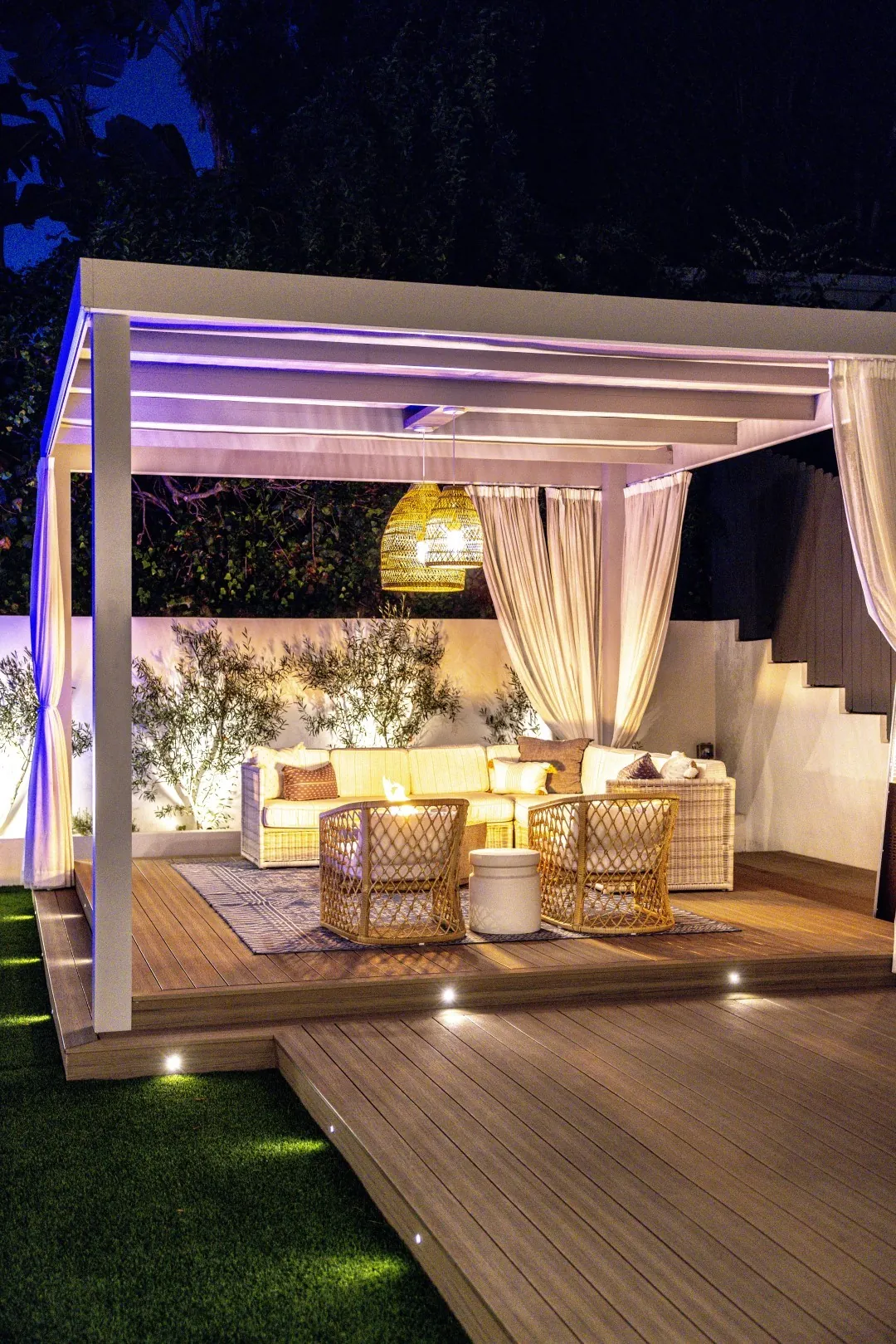 Sheens Project cabana pergola at night with sheer curtains, a woven pendant light, and lounge chairs on the lit deck in Los Angeles