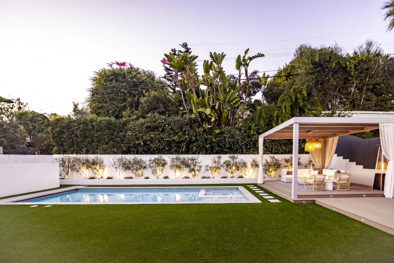 Sheens Project white cabana pergola with sheer curtains beside the pool and uplit olive tree planter in Los Angeles