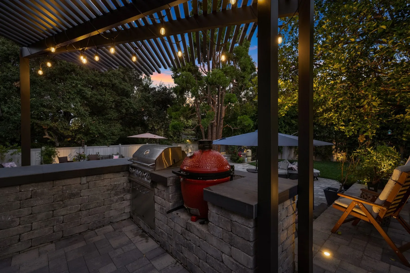 Black louvered pergola with string lights over an outdoor kitchen with a stone veneer island and grills in Pasadena