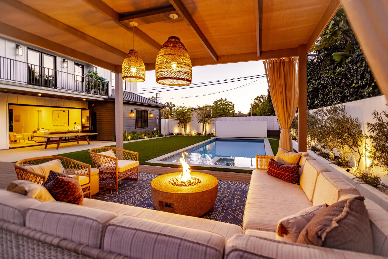 Sheens Project pergola lounge with woven pendant lights, an outdoor sectional, and a fire pit overlooking the pool in Los Angeles