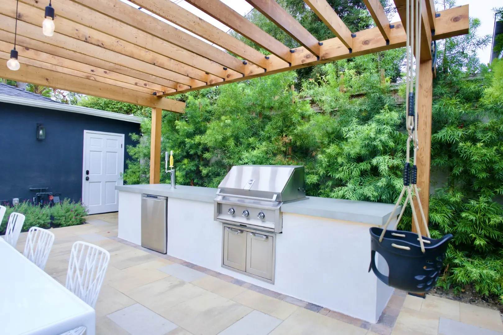 Agnew Project outdoor kitchen with a built-in grill and refrigerator under a wood pergola on a stone paver patio in Los Angeles
